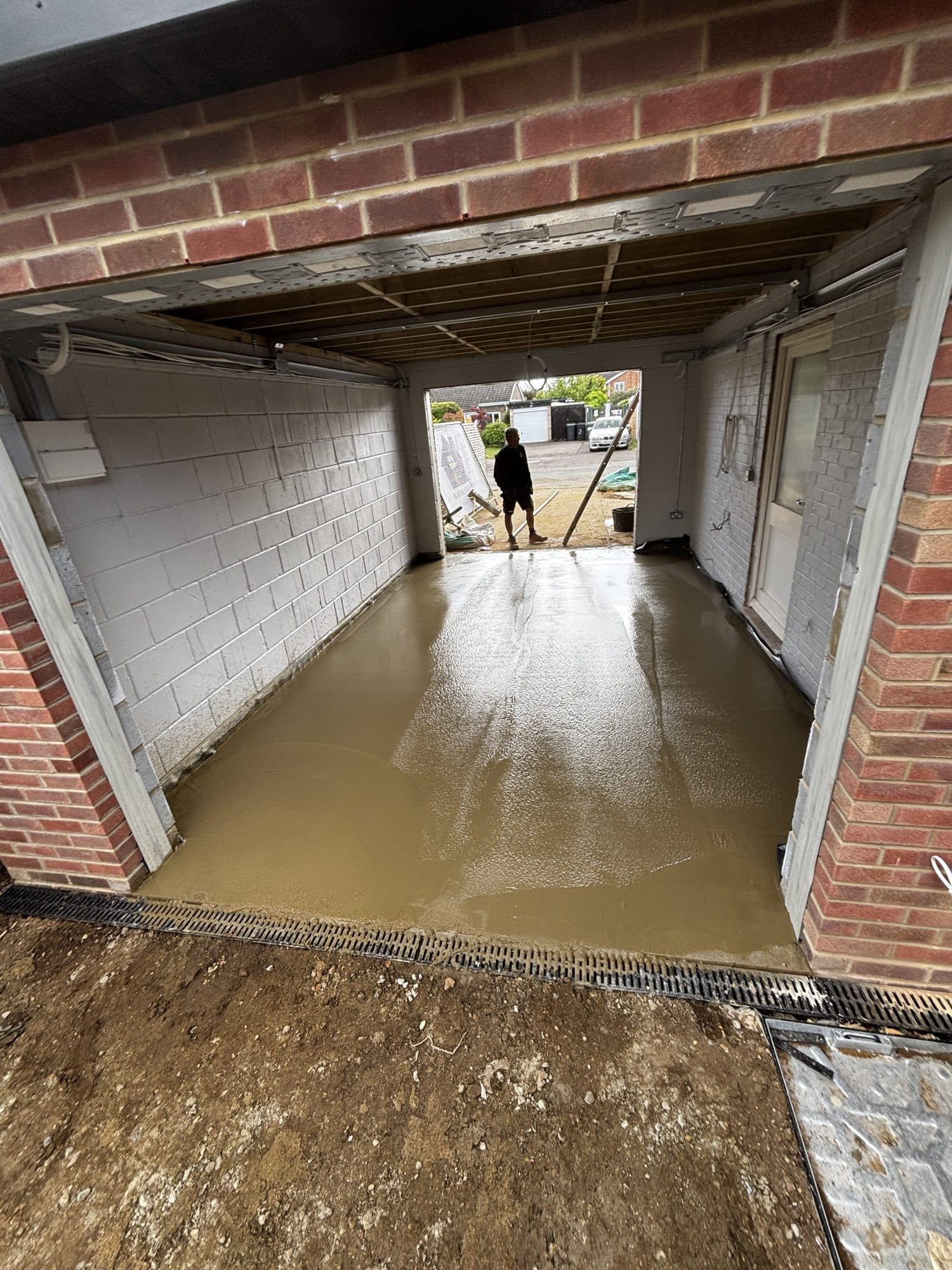Garage floor with wet concrete screed newly poured and a worker standing in the open doorway