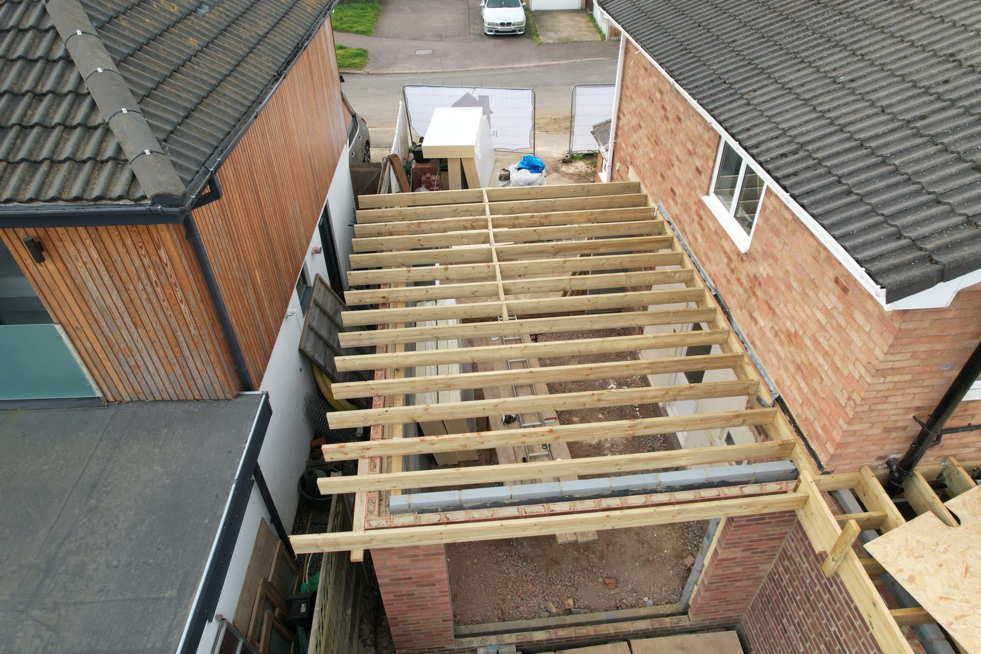 Aerial view of new timber roof joists laid across the flat roof extension between neighbouring houses