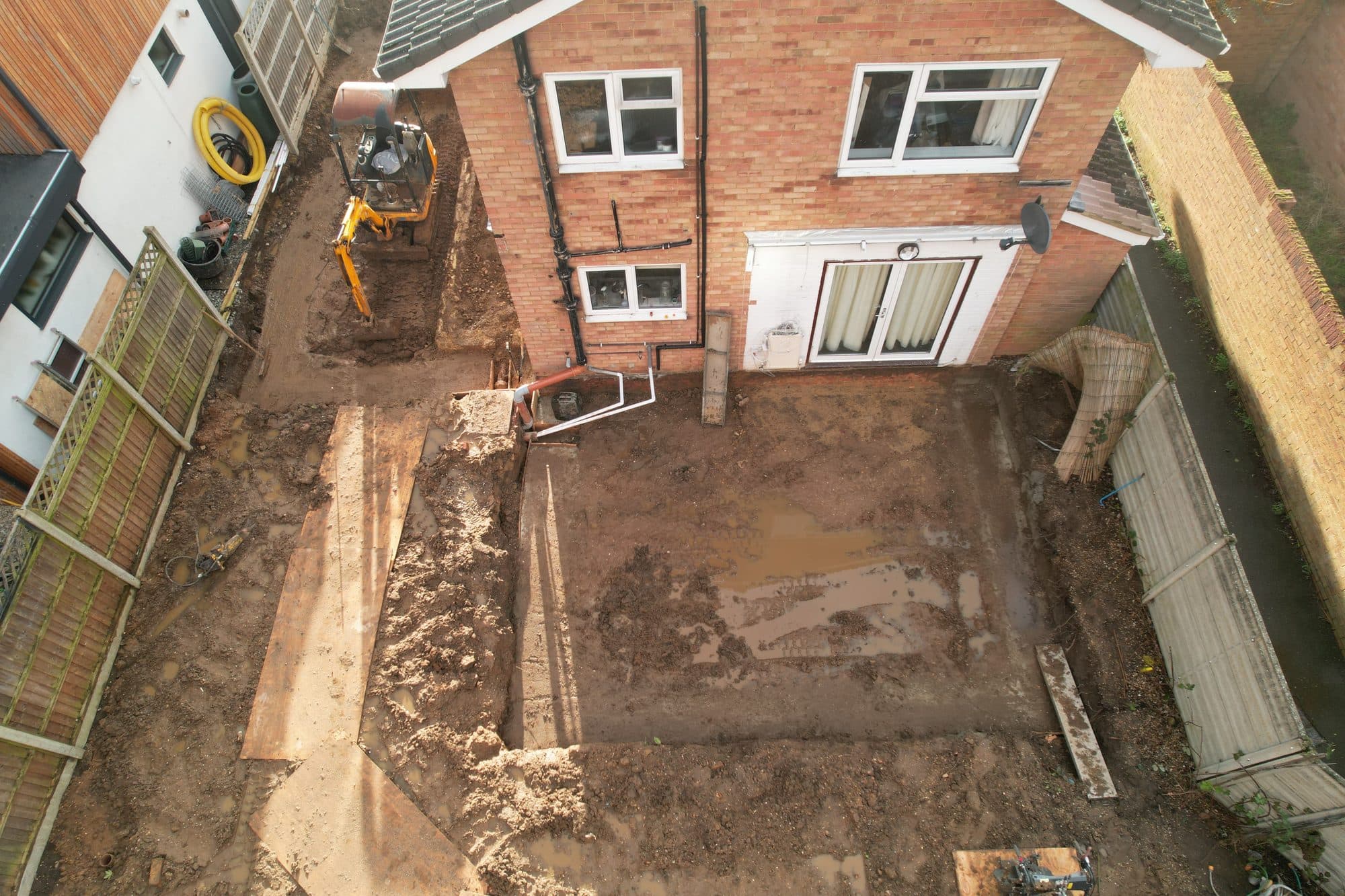 Aerial view of the excavated foundation trenches for the extension, with a mini digger and the rear of the house above