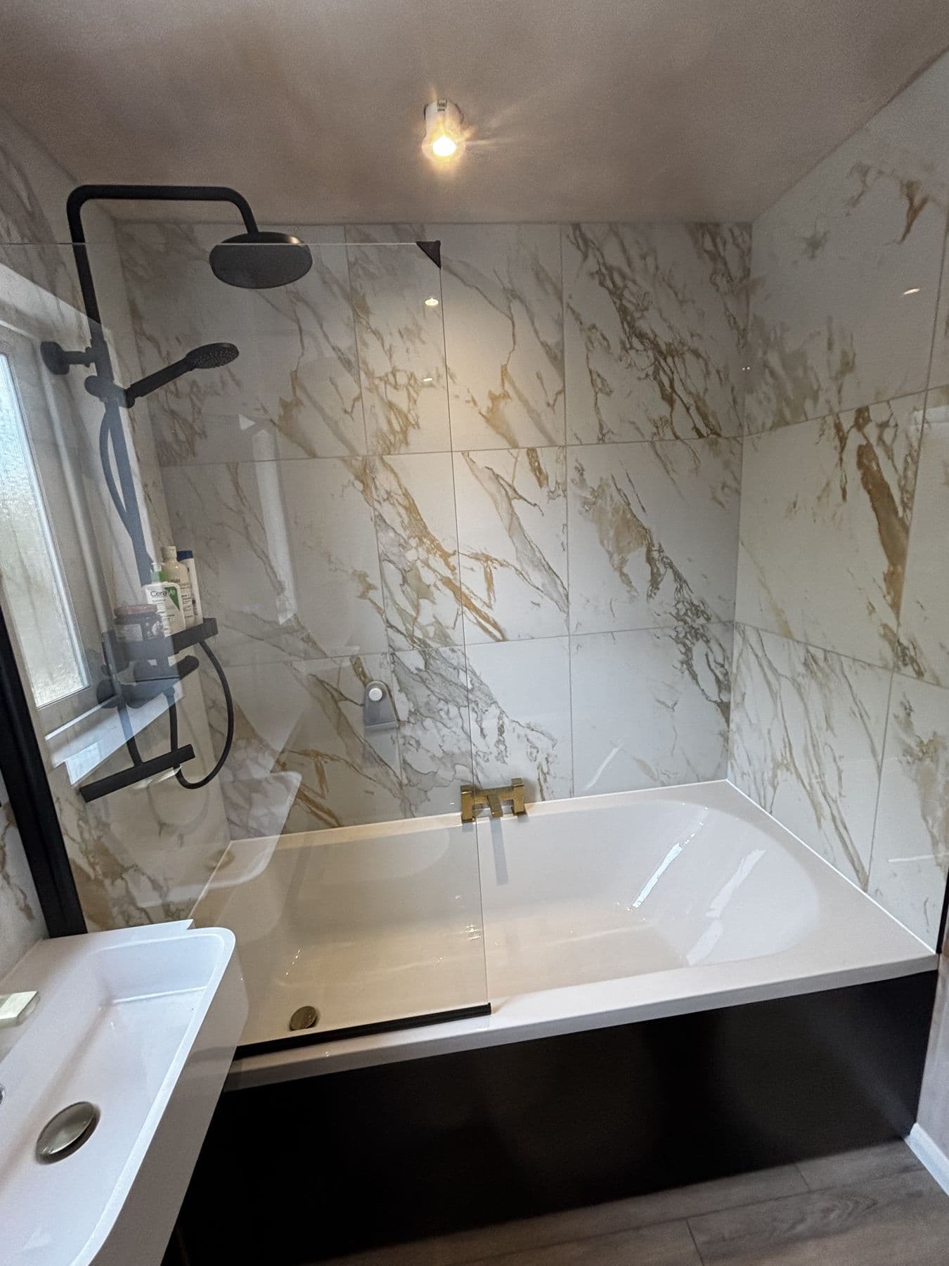 Bath with black shower fixtures, marble tiled walls and gold bath taps