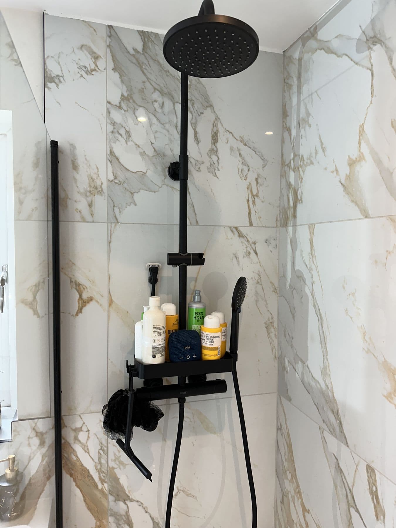 Black overhead shower and riser rail against marble tiled wall in the shower corner