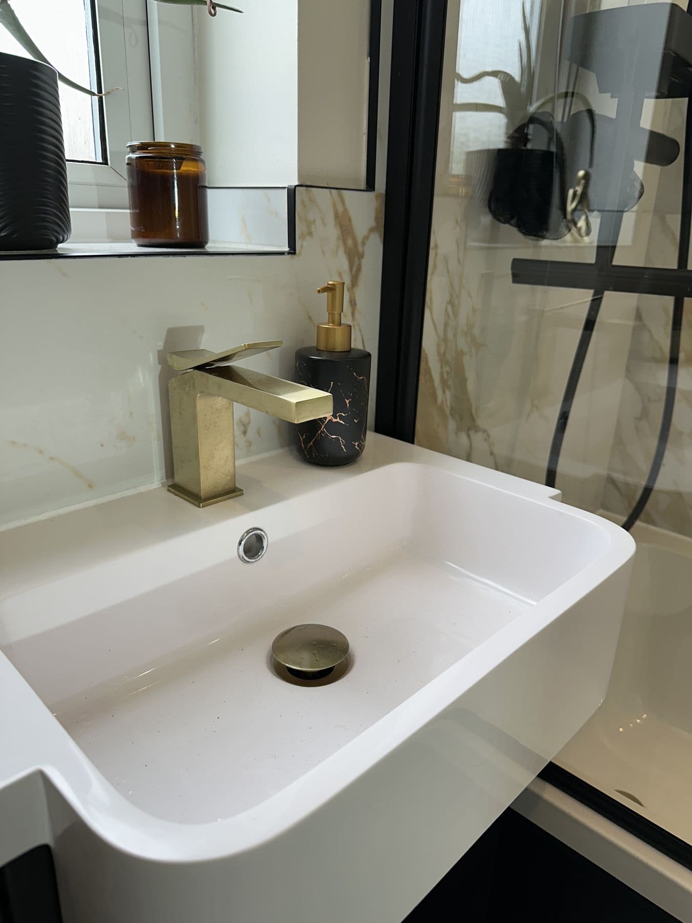 Close up of sink with gold tap, gold pop up waste and black marble soap dispenser
