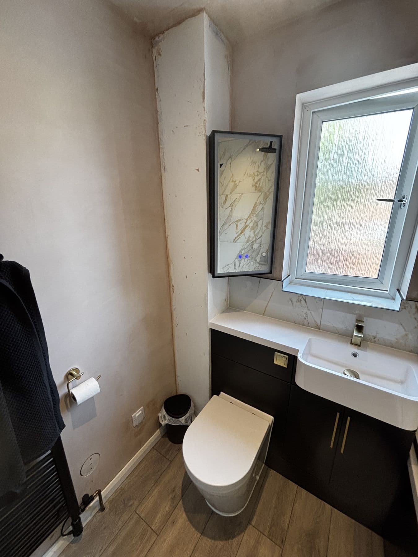 Black vanity unit with mirrored cabinet and sink beneath a window, toilet alongside