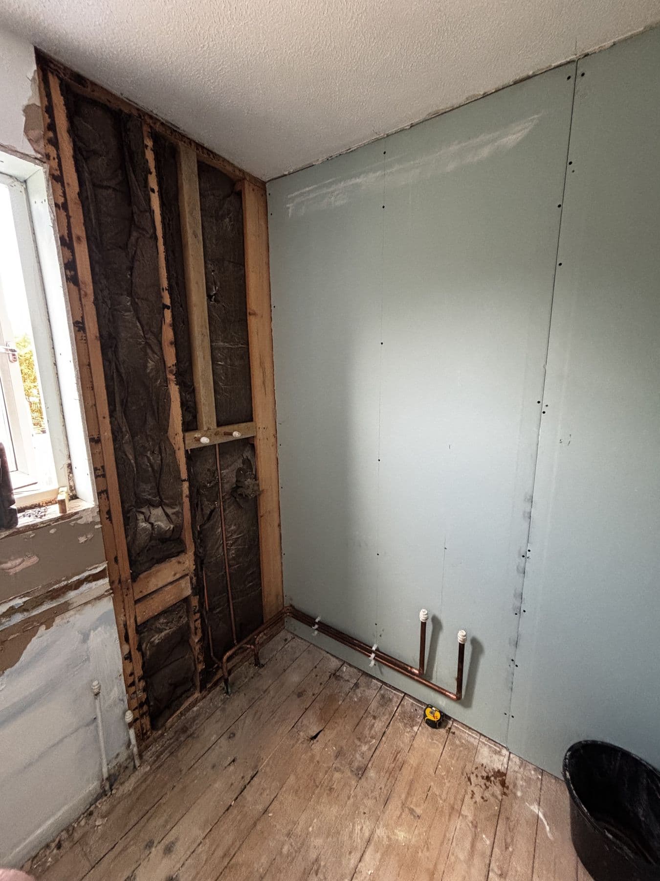 Bathroom wall stripped back to studwork and insulation with copper pipework exposed during renovation
