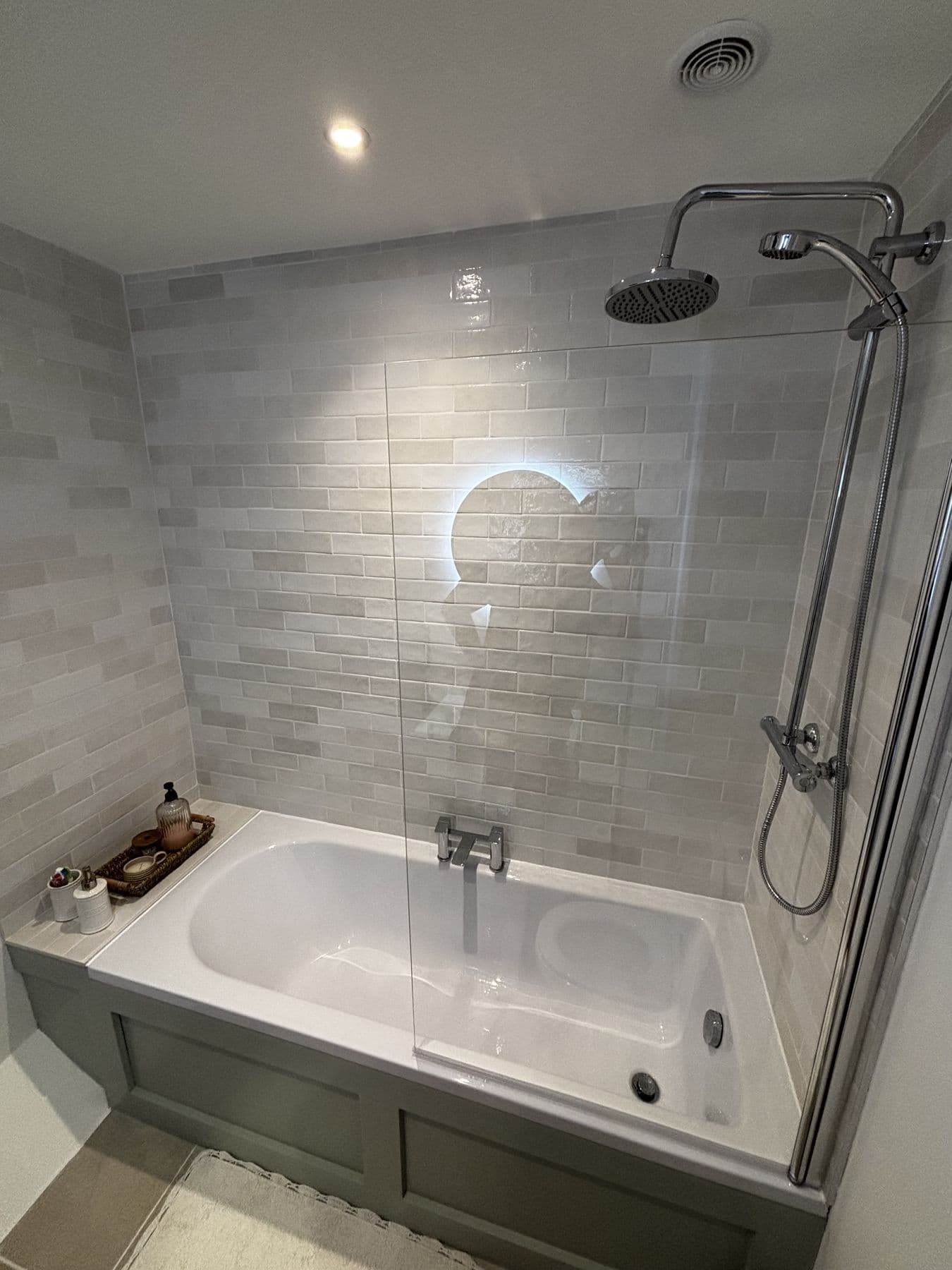 Bath with glass shower screen, chrome rainfall shower and brick-effect tiled walls in soft grey and cream tones