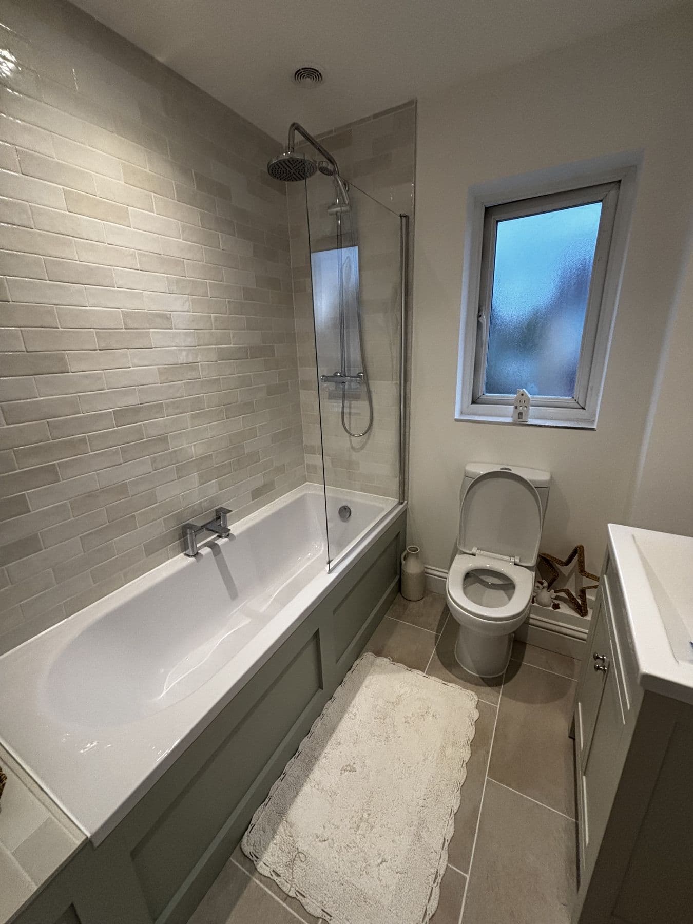Bath and shower combination with chrome fittings, toilet and frosted window, grey brick-effect tiled walls