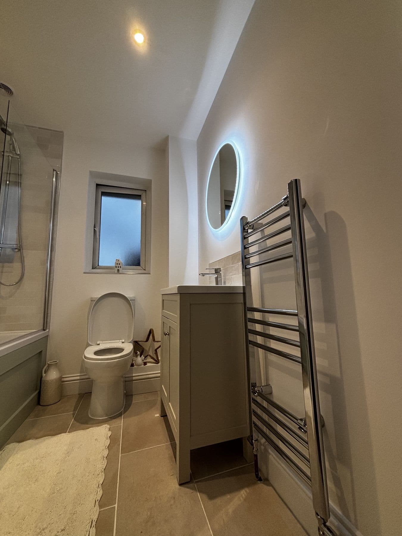 Toilet, vanity basin with illuminated round mirror and chrome ladder towel rail