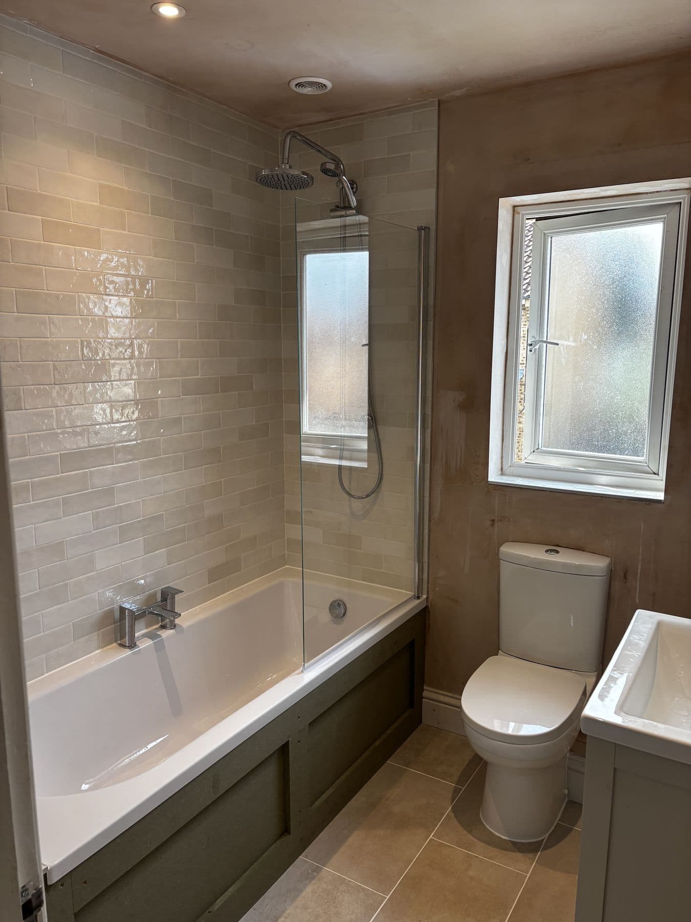 Bath and shower fitted with tiling complete on one wall, the opposite wall still bare plaster awaiting finishing, mid-renovation