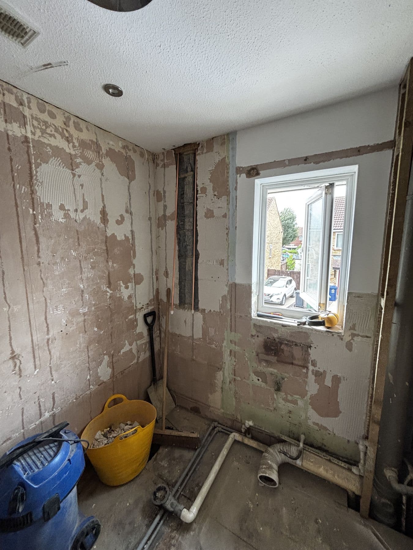 Bathroom stripped back to bare plaster and exposed pipework, mid-renovation with tools and rubble on the floor