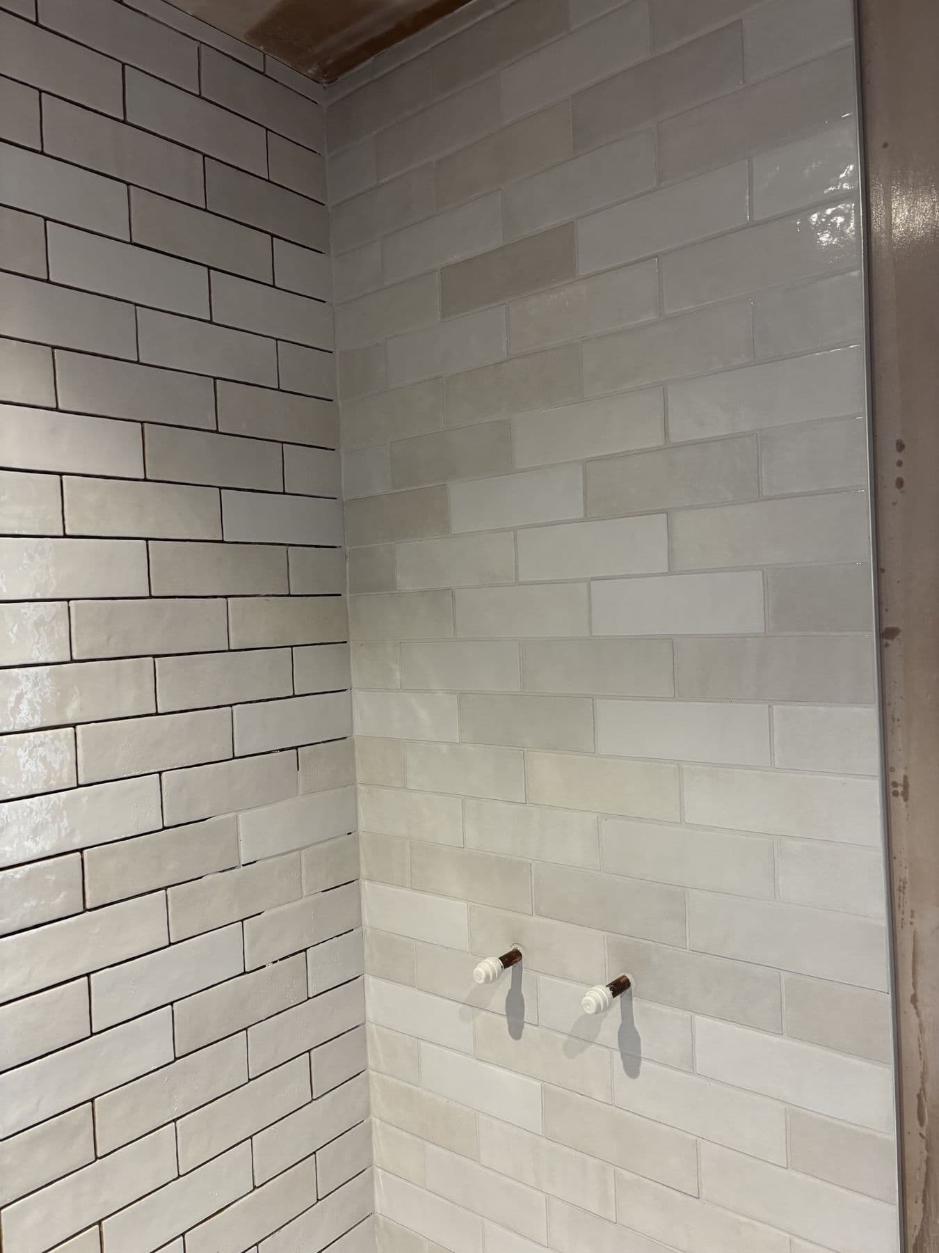Close-up of brick-effect wall tiling partway through installation, corner of the shower area
