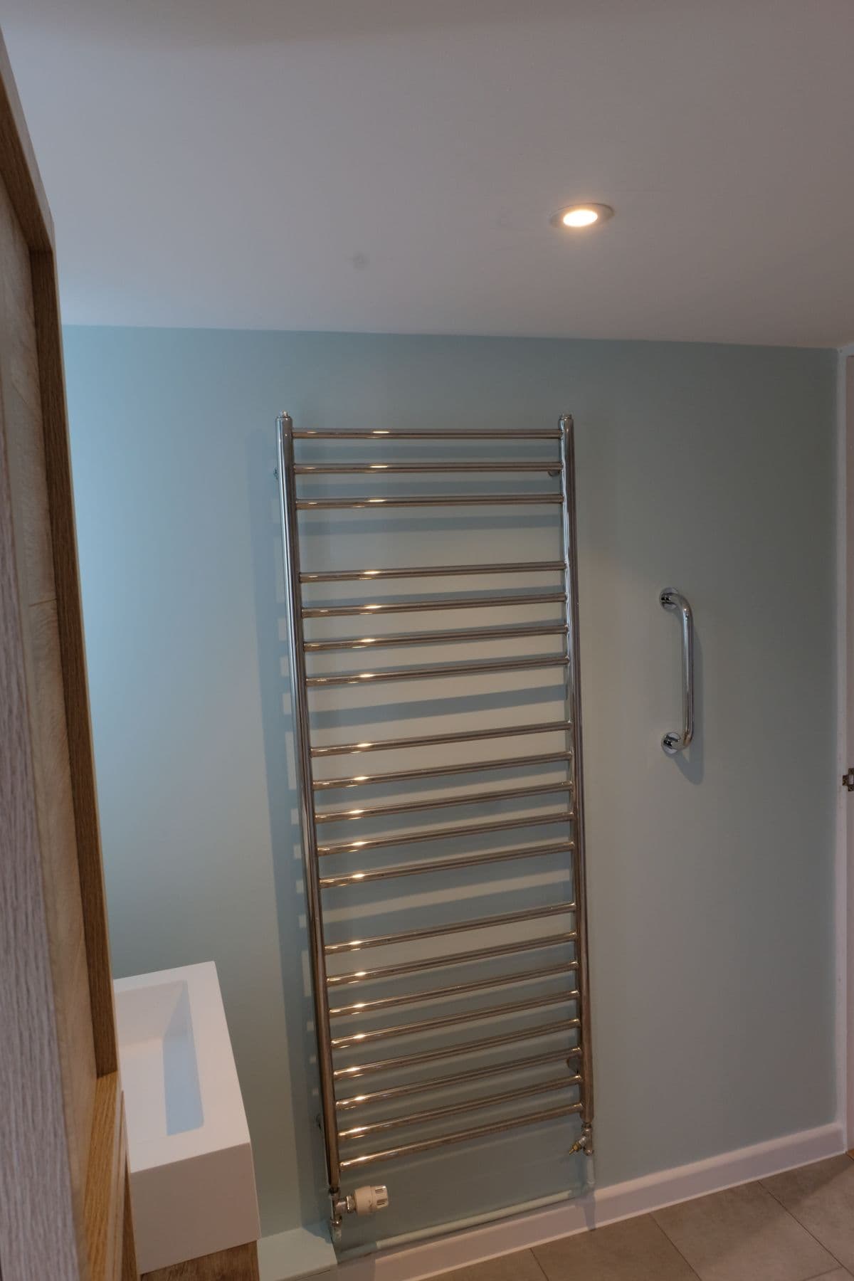 Chrome ladder towel radiator and grab rail on a pale blue wall