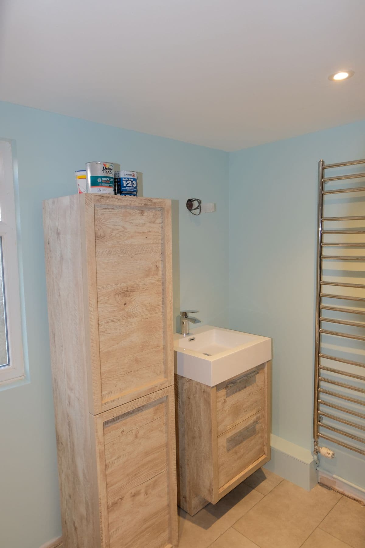 Wood effect tall storage cabinet beside a small wall hung sink with chrome tap