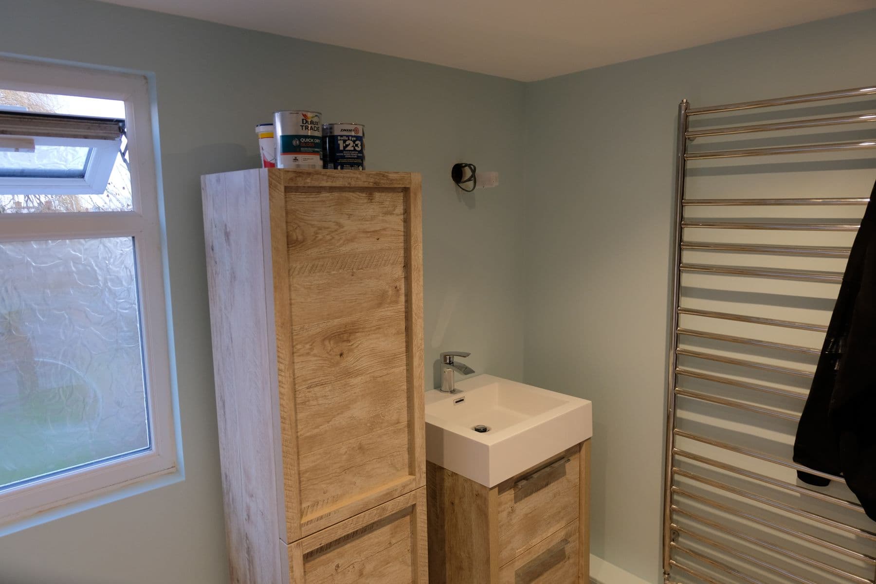 Wood effect bathroom cabinet and wall hung sink next to a chrome ladder towel radiator