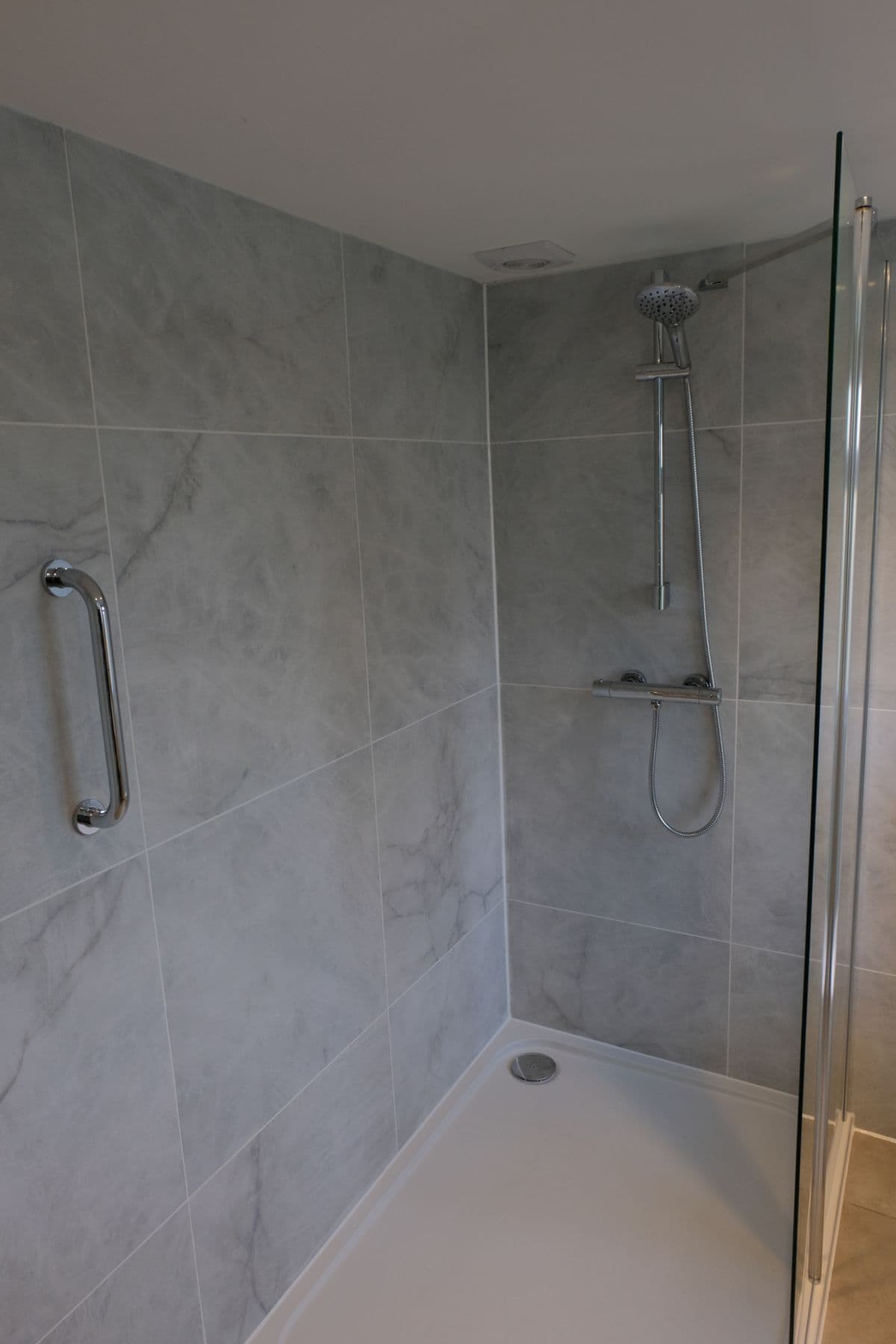 Shower cubicle with grey tiling, chrome grab rail and chrome shower riser rail