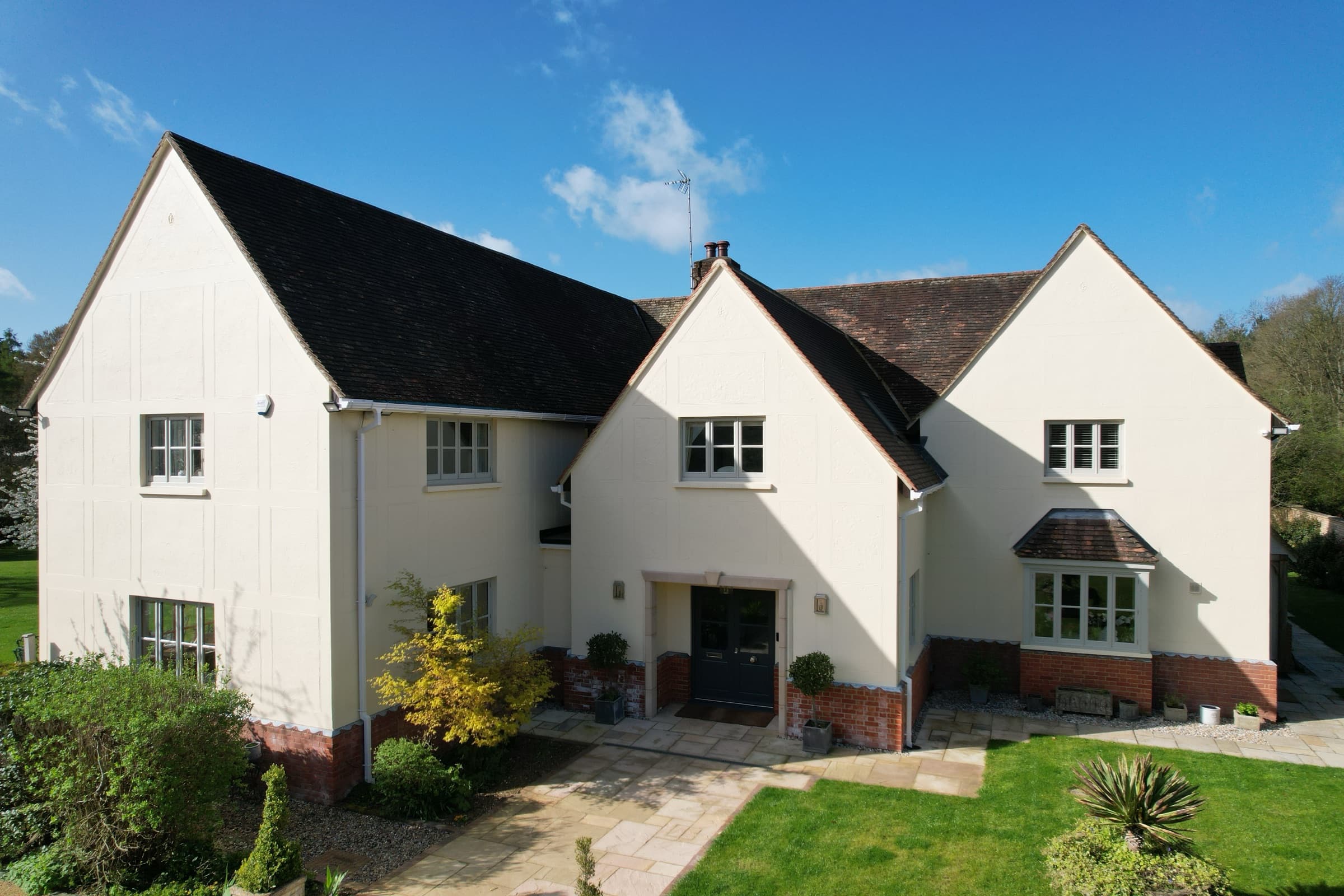 Aerial view of a large rendered house with multiple gabled roofs, dark roof tiles and red brick base, Ayot St Lawrence, Hertfordshire