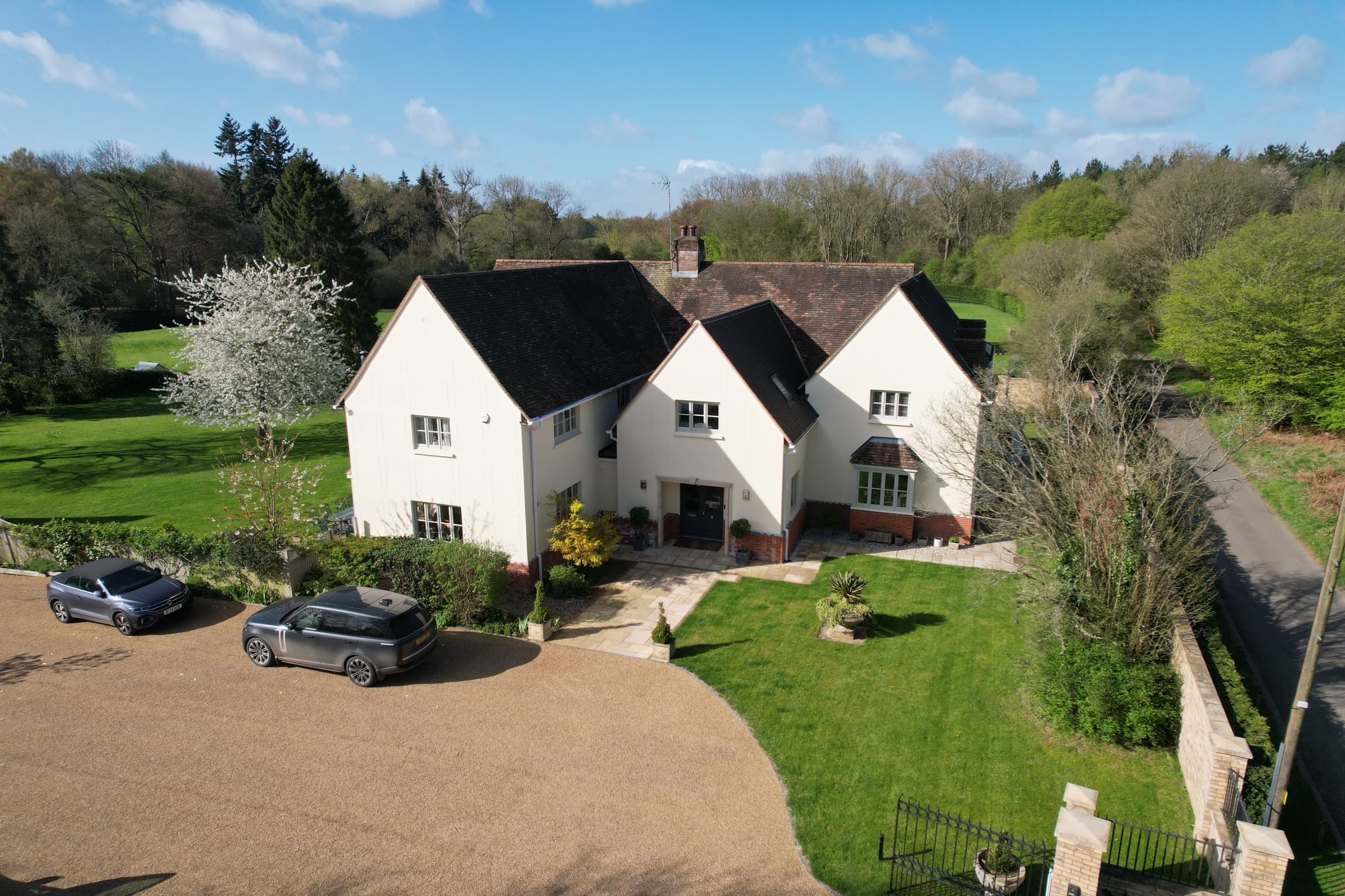 Aerial view of the house's entrance with two cars parked on the gravel driveway and lawned gardens