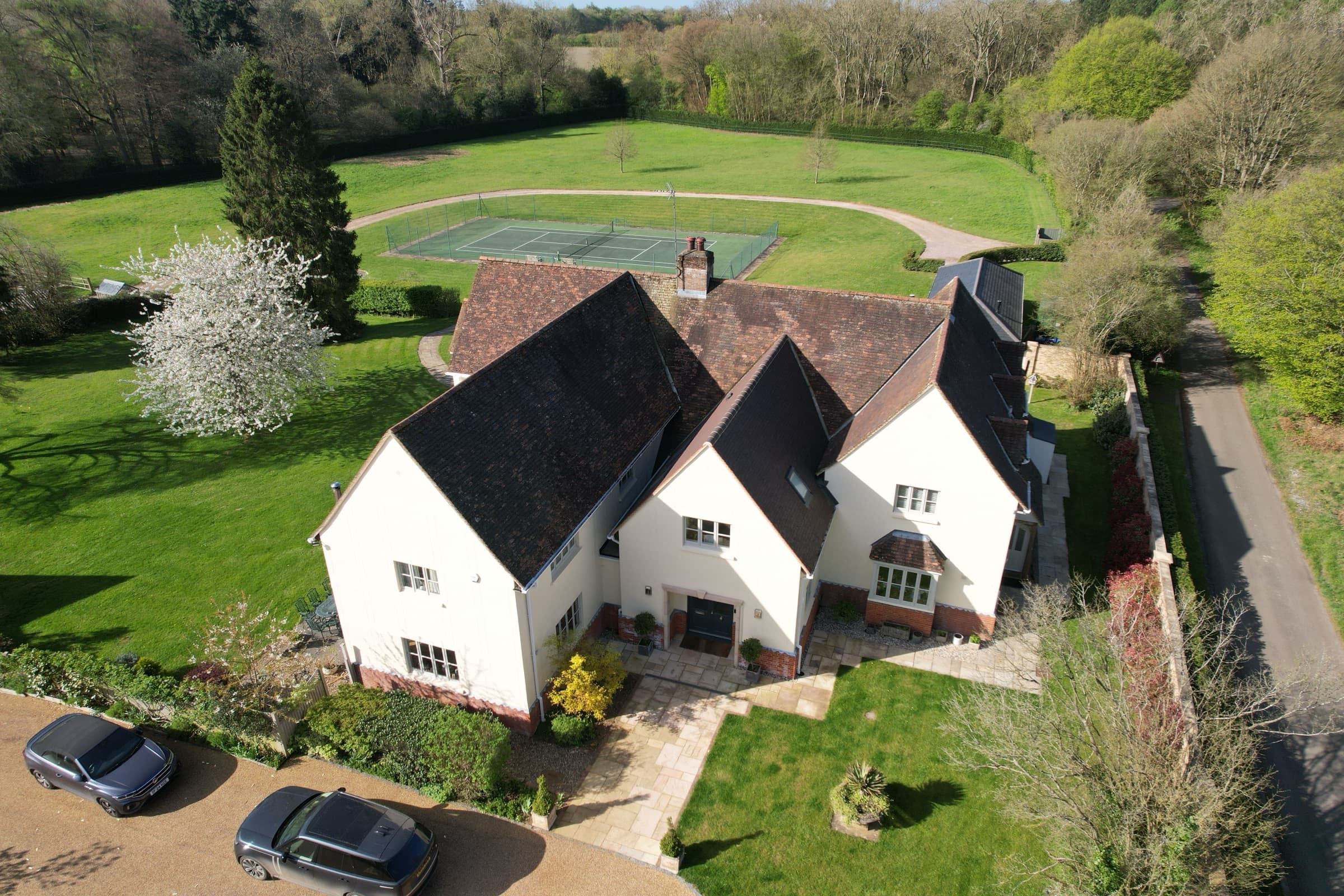 Aerial view of the house and gardens showing a tennis court bordered by woodland