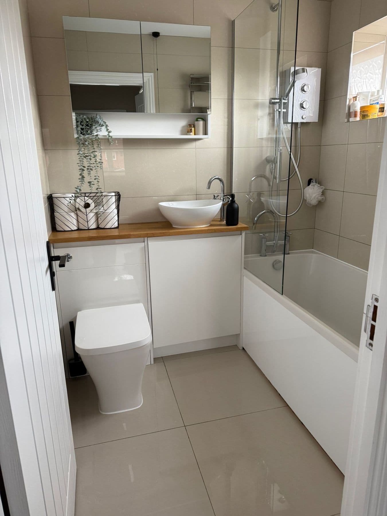 Bathroom with a white wall-hung basin on an oak topped vanity unit, mirrored cabinet above and a bath with glass shower screen