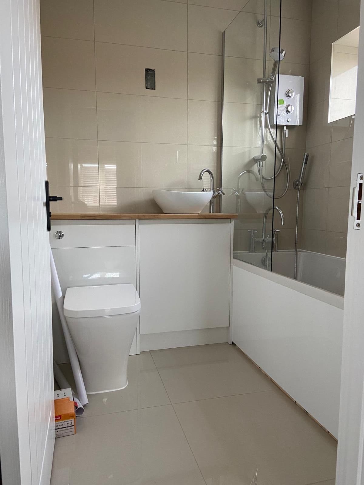 Bathroom with a white countertop basin on an oak topped vanity unit, close coupled toilet and a bath with glass shower screen and chrome fittings