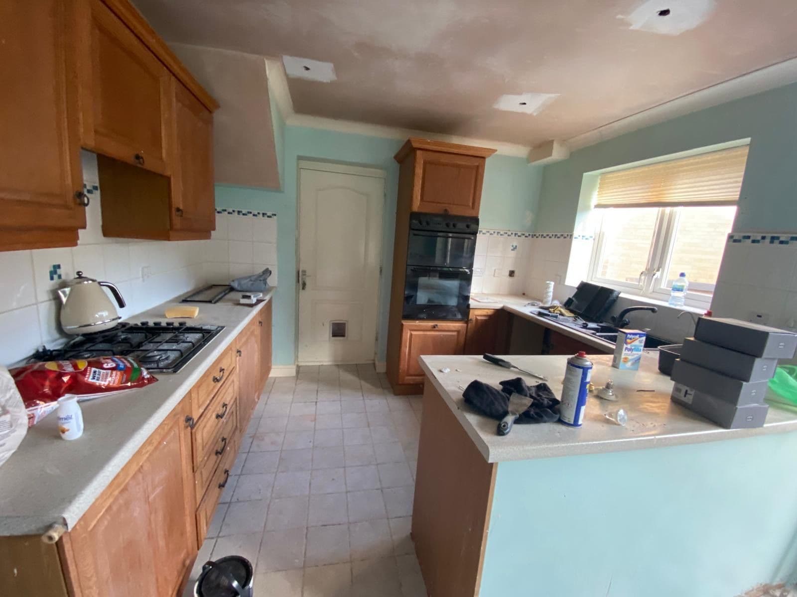 Original kitchen before renovation with oak effect cabinets, teal painted walls, a gas hob and floral tiled splashback