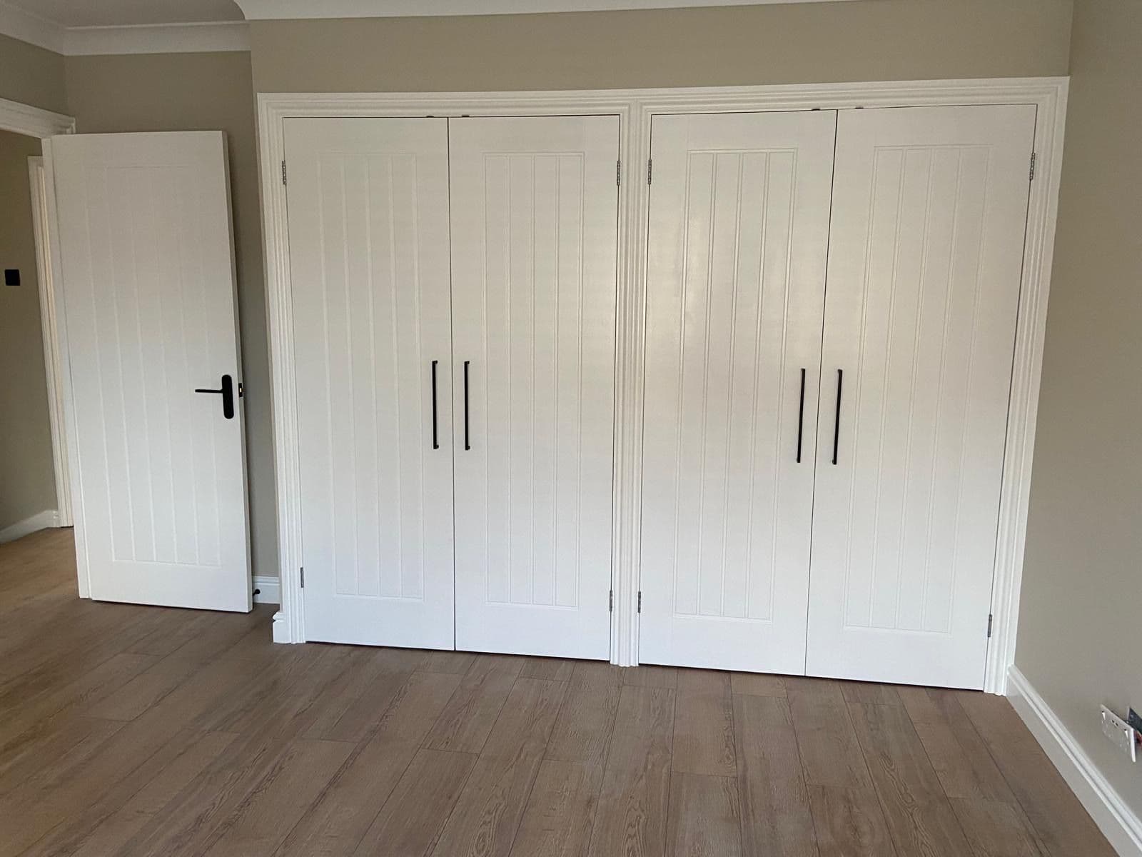 Fitted bedroom wardrobes with white panelled double doors, black handles and wood effect flooring