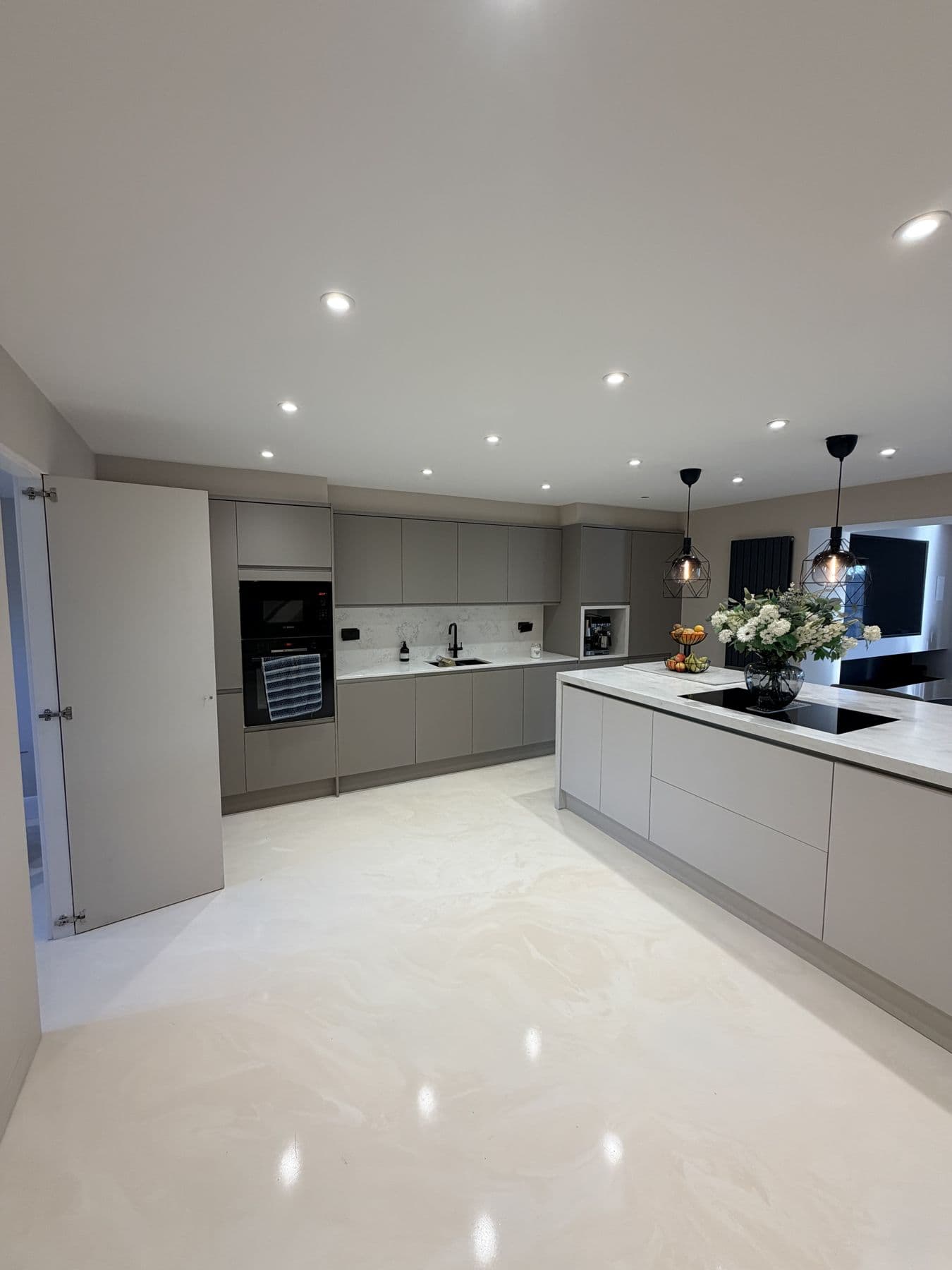 Open-plan kitchen with light grey handleless cabinetry, white marble effect worktops, a central island with black induction hob and geometric wire pendant lights, Gaunts Way, Letchworth