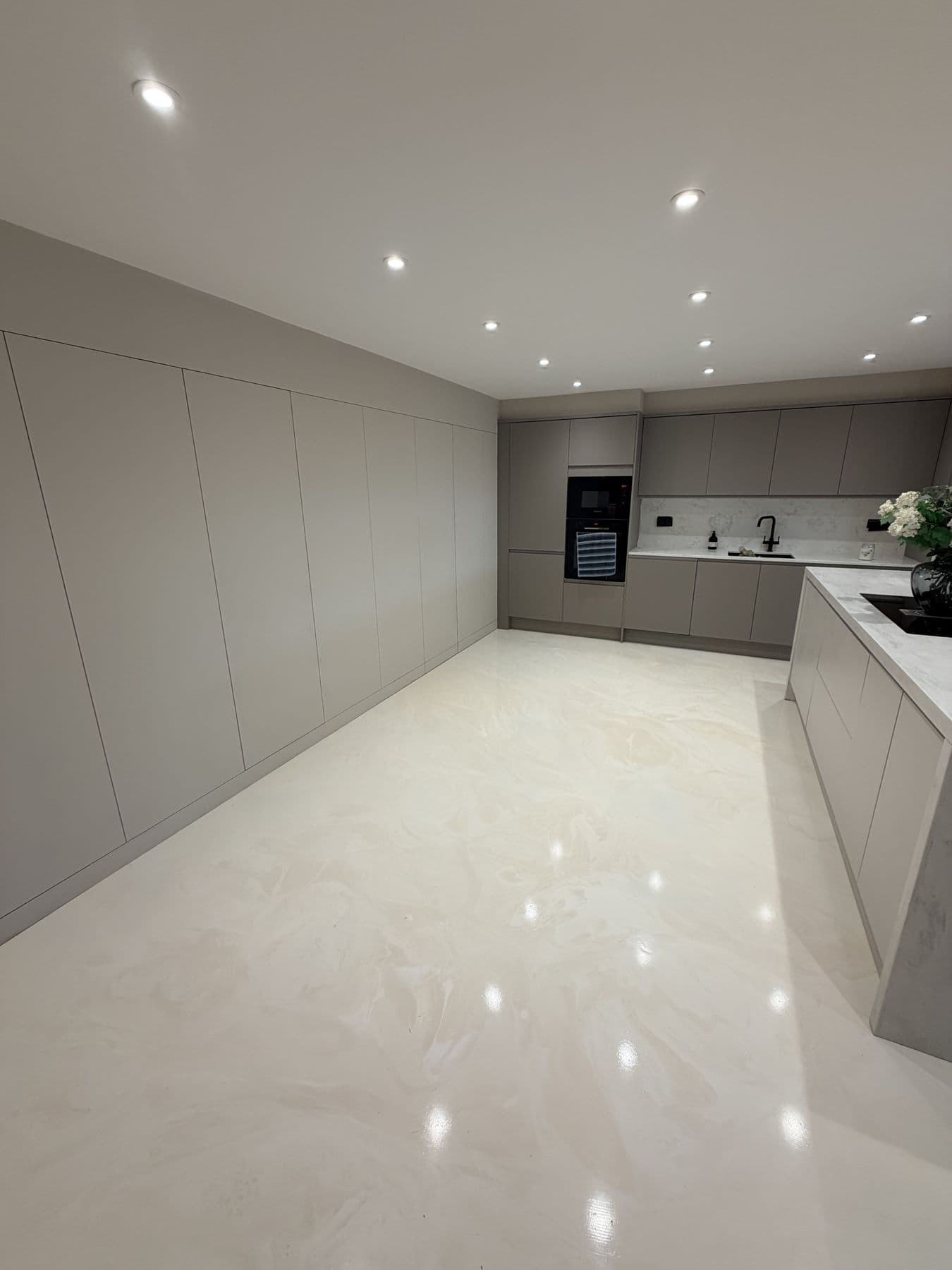 Light grey kitchen with full height cabinetry along one wall, integrated oven and microwave, and a view through to the island and sink area