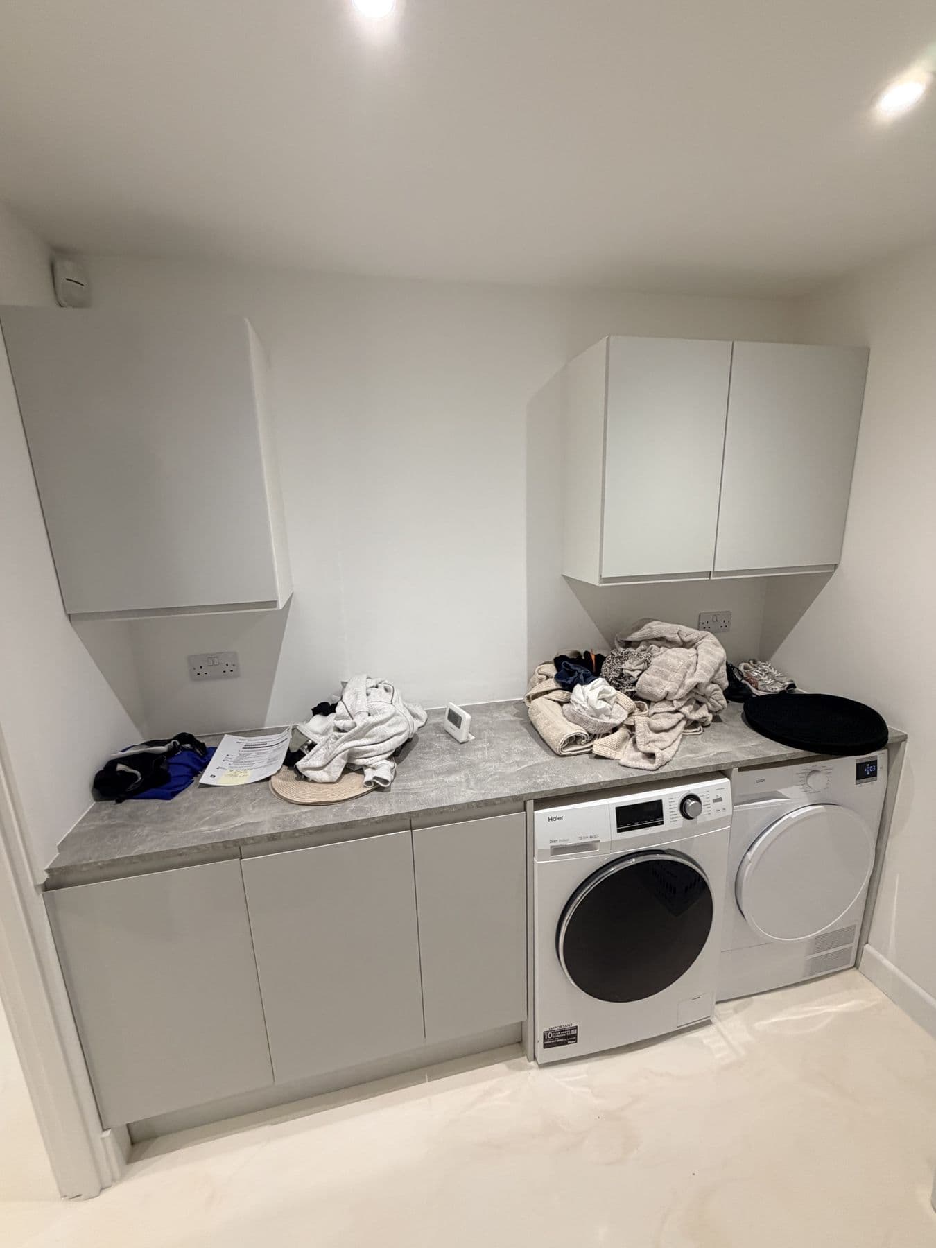 Utility room with wall mounted cabinets, a grey marble effect worktop with laundry on it, washing machine and tumble dryer