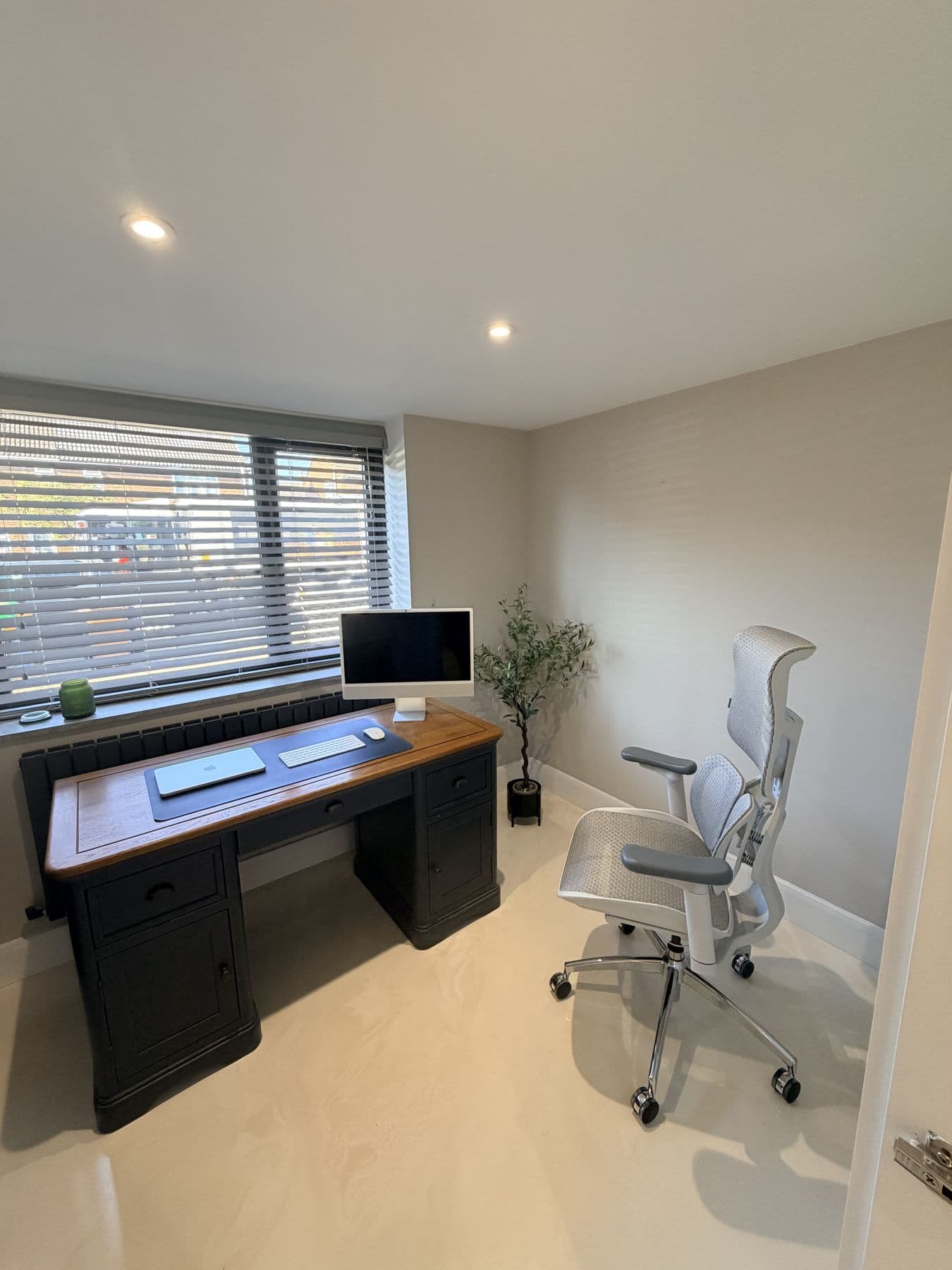 Home office with a dark wood topped desk, iMac, white ergonomic mesh desk chair and a window with striped blinds