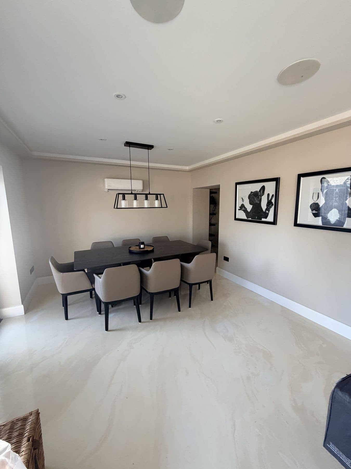 Dining room with a dark wood table, eight grey upholstered chairs, black framed artwork and a black pendant light fitting