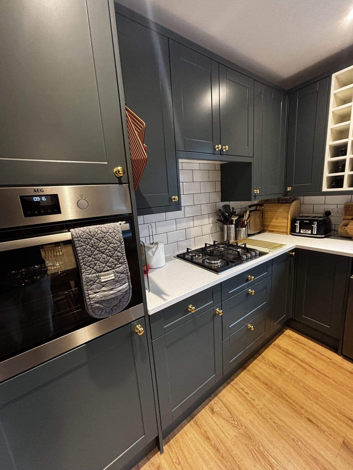 Shaker style dark green kitchen with brass handles, white quartz worktops, metro tile splashback and gas hob, built-in AEG oven to the side, High Street, Henlow