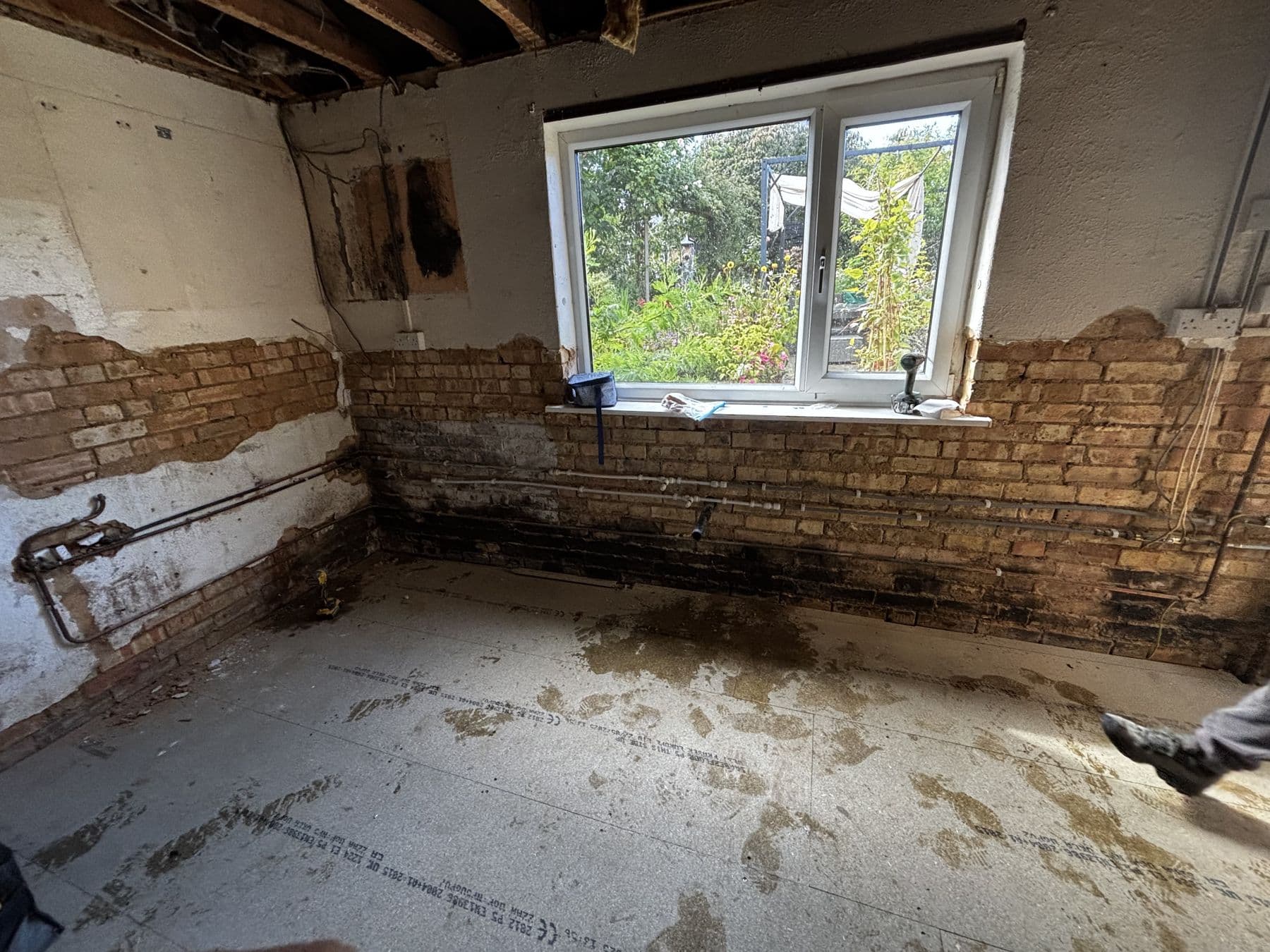 Kitchen stripped back to bare brick and old pipework during strip out, with damp staining on the lower walls