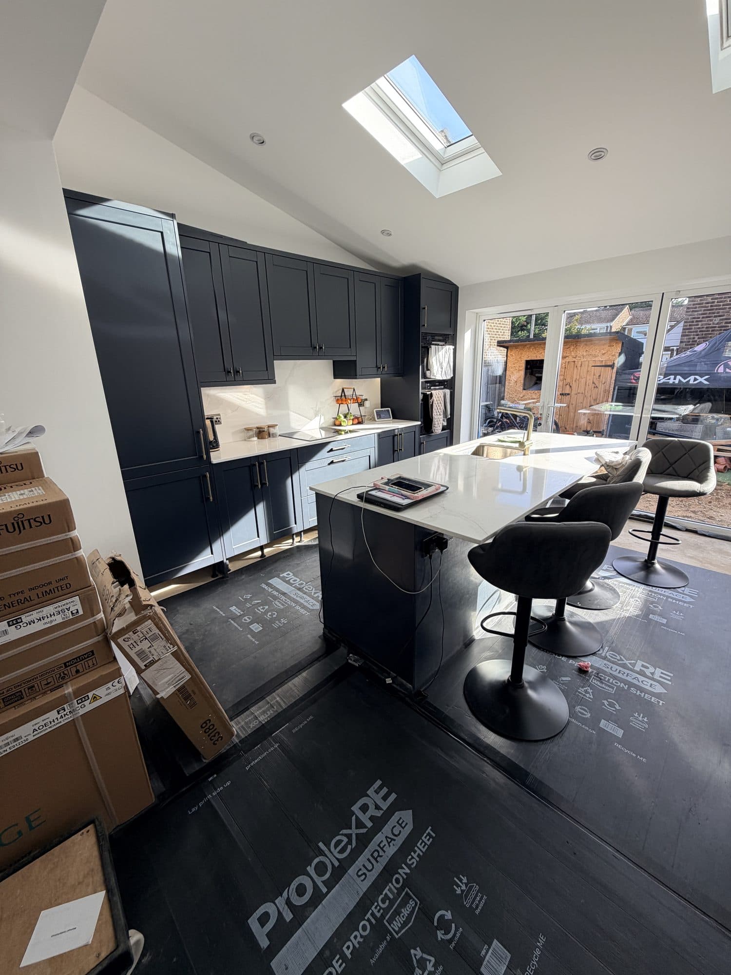 Open-plan kitchen extension during fit out, with navy blue shaker cabinets, a central island, roof light and bifold doors onto the garden, protective floor covering still down, Holly Close, Biggleswade