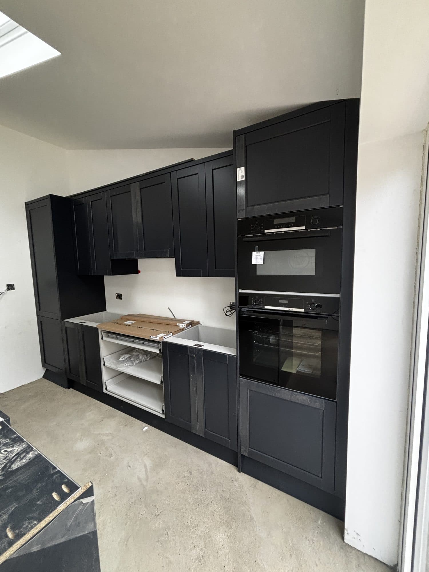 Navy blue kitchen cabinetry under construction, with built in double ovens, drawers pulled out and the worktop still protected