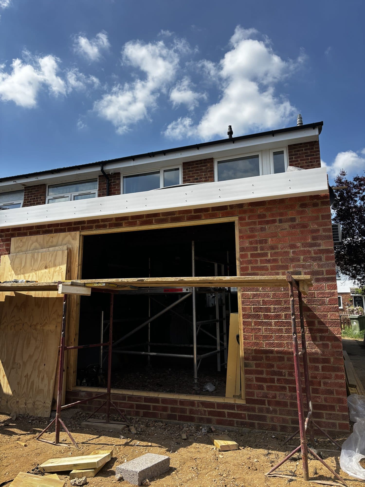 Rear elevation of the house showing new brickwork for the extension with a window opening framed in and scaffold boards still in place