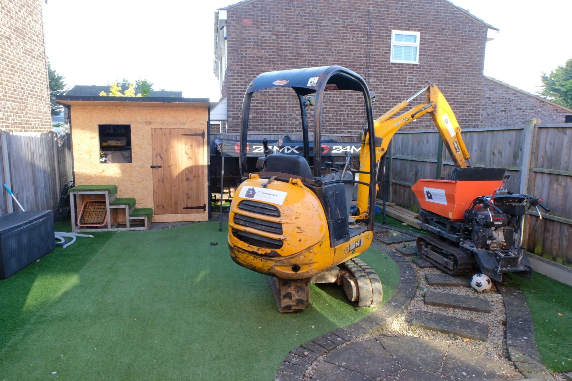 Back garden of the house with a mini digger and a tracked dumper on site next to a timber shed