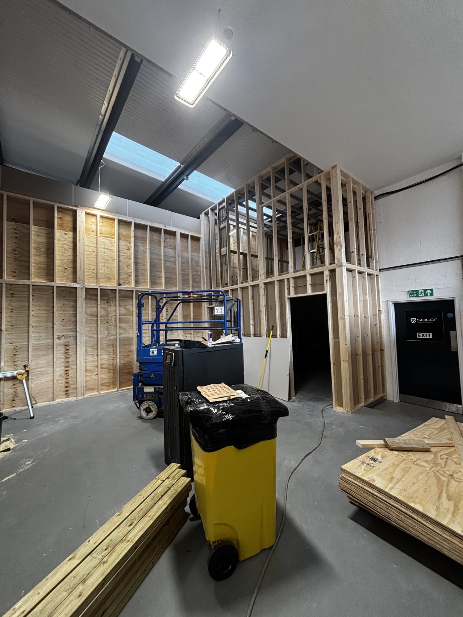 Office fit out at Eldon Way, Biggleswade during construction with timber stud walls, a scissor lift and stacked plywood sheets