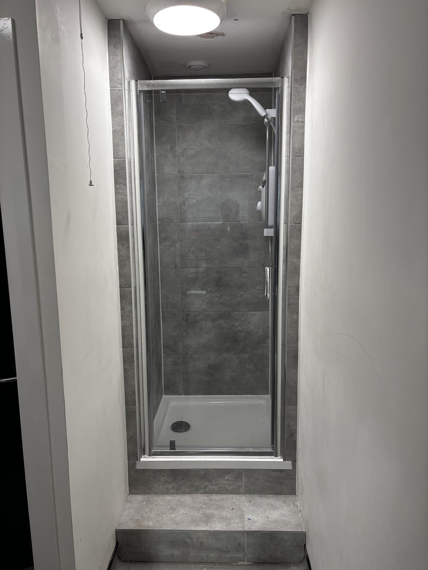 Finished shower cubicle with a glass door, tiled walls and a wall mounted shower