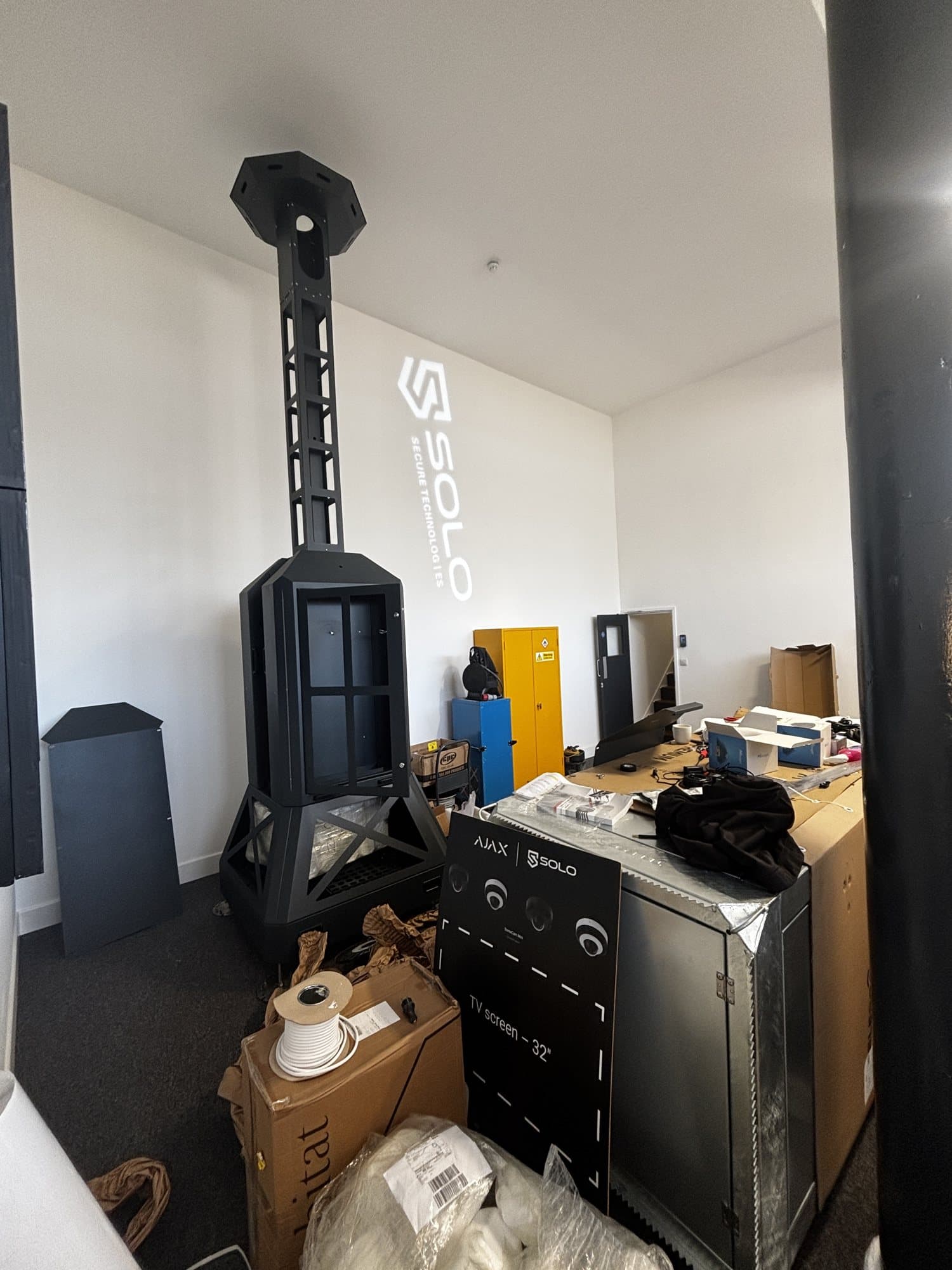 Finished room with a tall black security equipment tower, yellow and blue storage cabinets and the SOLO logo projected on the wall