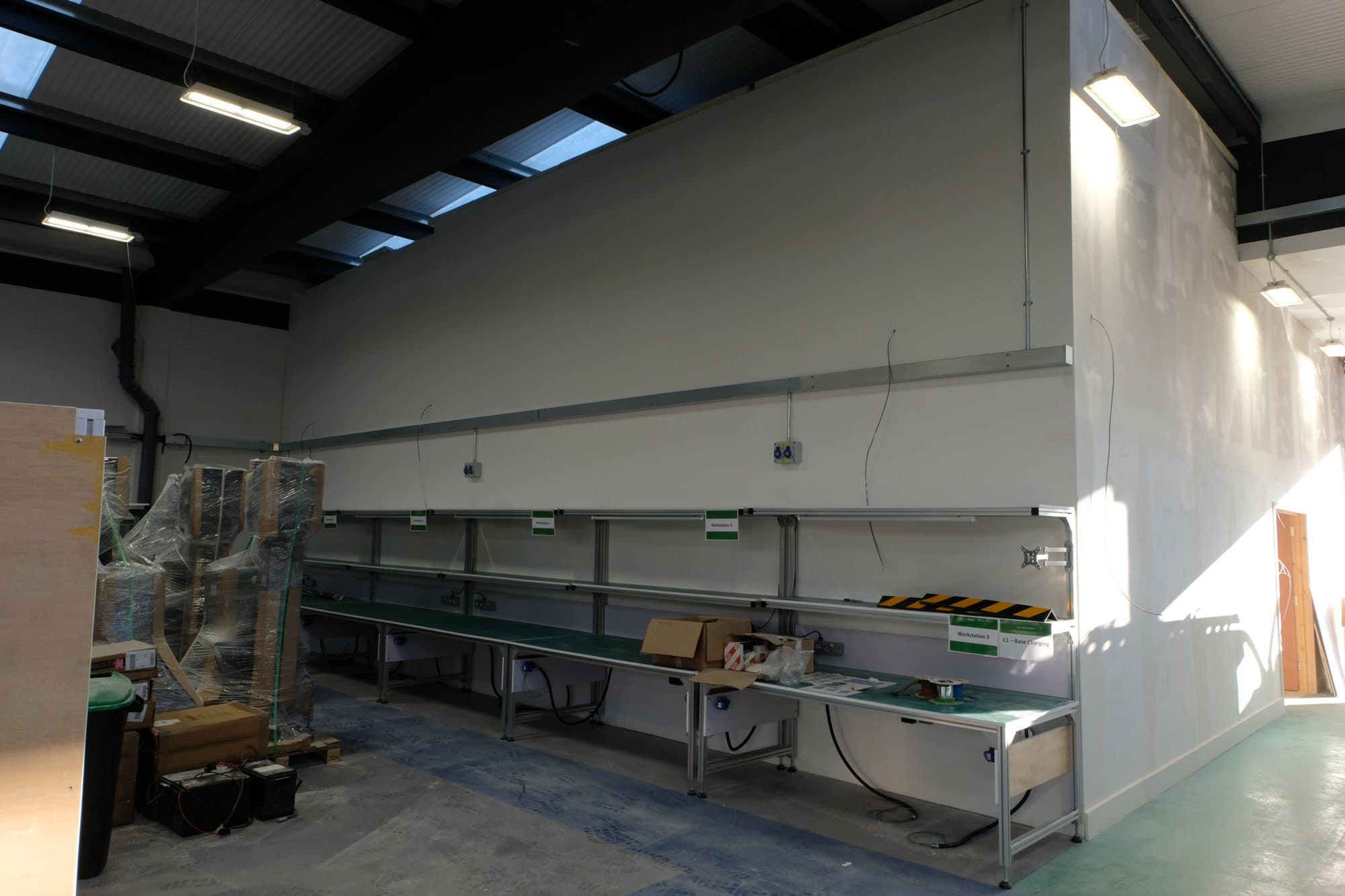 Finished warehouse area with workbenches, green work mats and labelled workstations along a partition wall