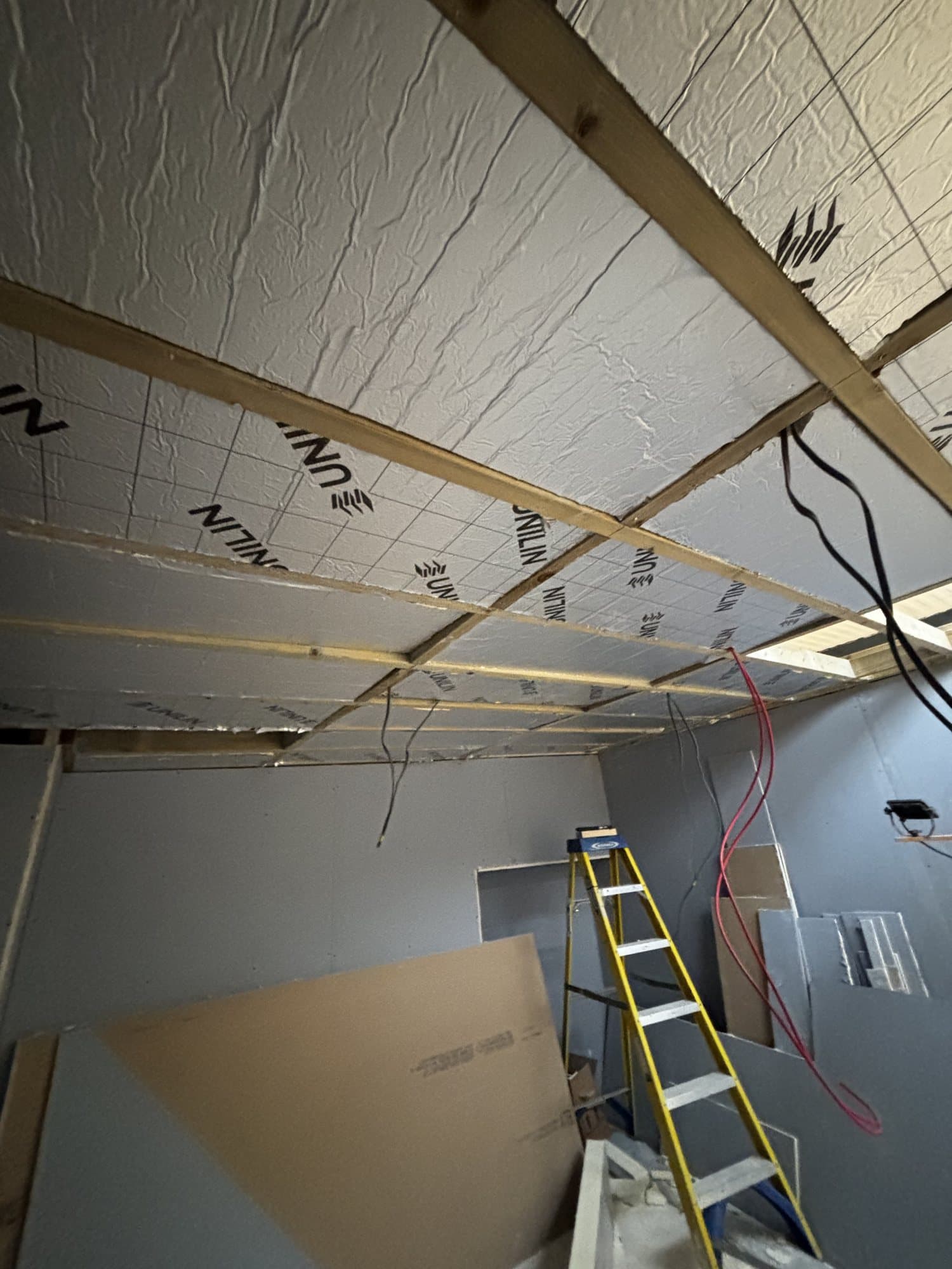 Ceiling insulation and timber joists exposed during first fix, with a ladder and loose wiring in an unfinished room