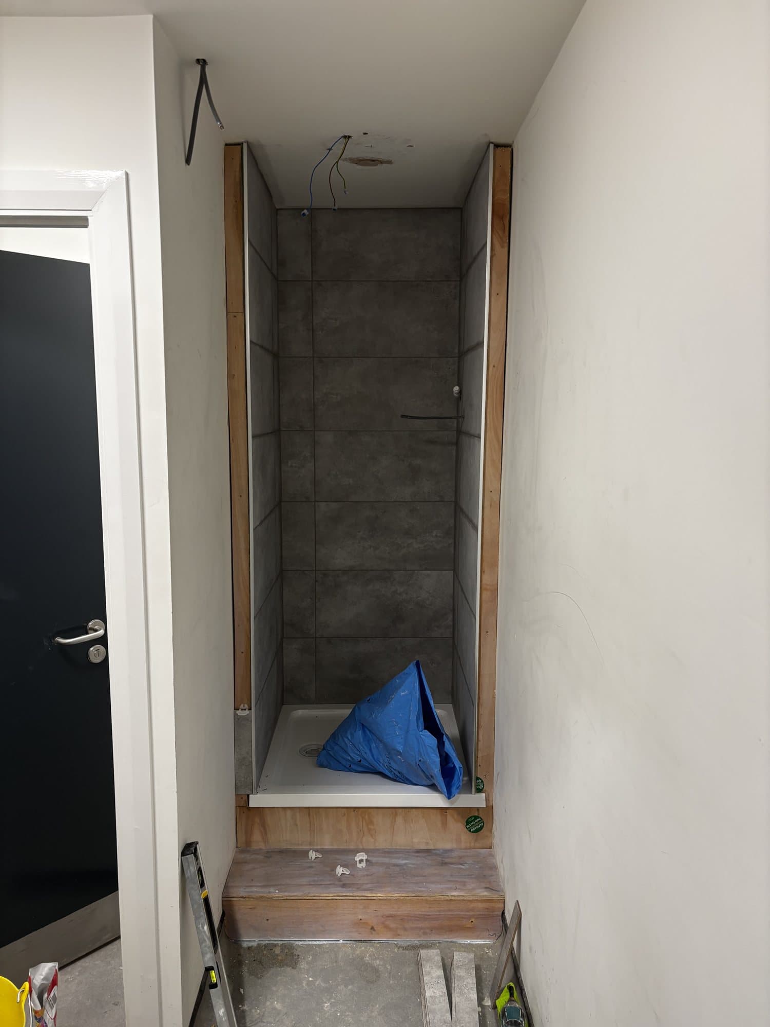 Shower cubicle being tiled with a shower tray fitted and wiring still hanging from the ceiling