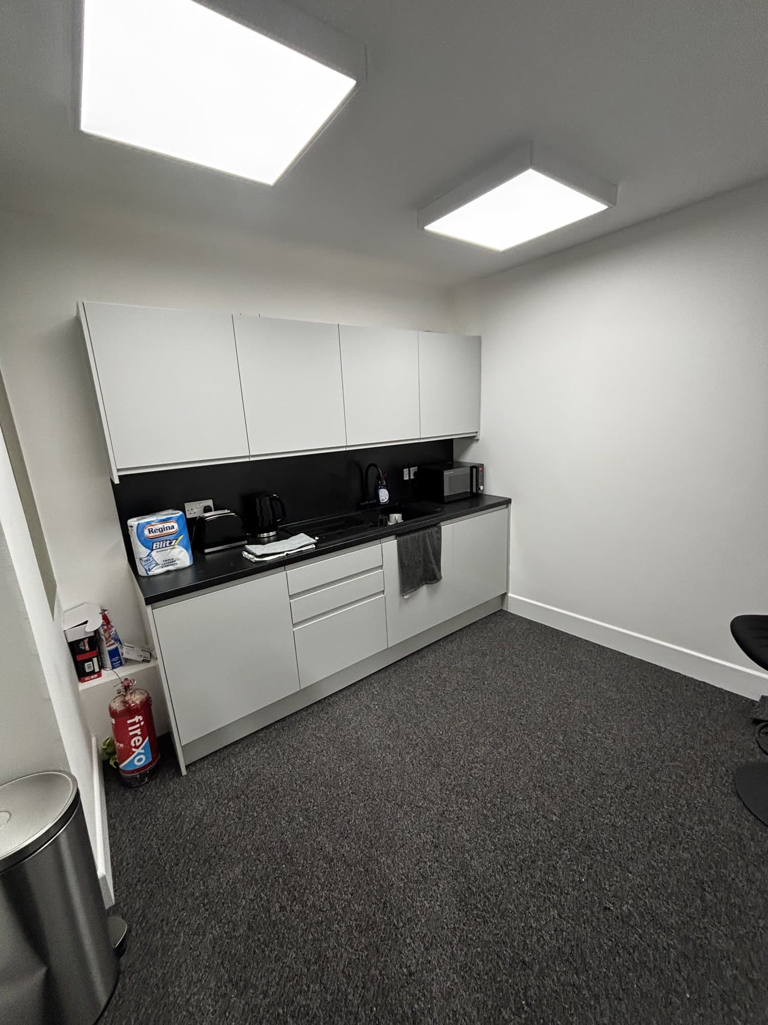 Finished kitchen with white cabinets, black countertop, sink, microwave, toaster and kettle