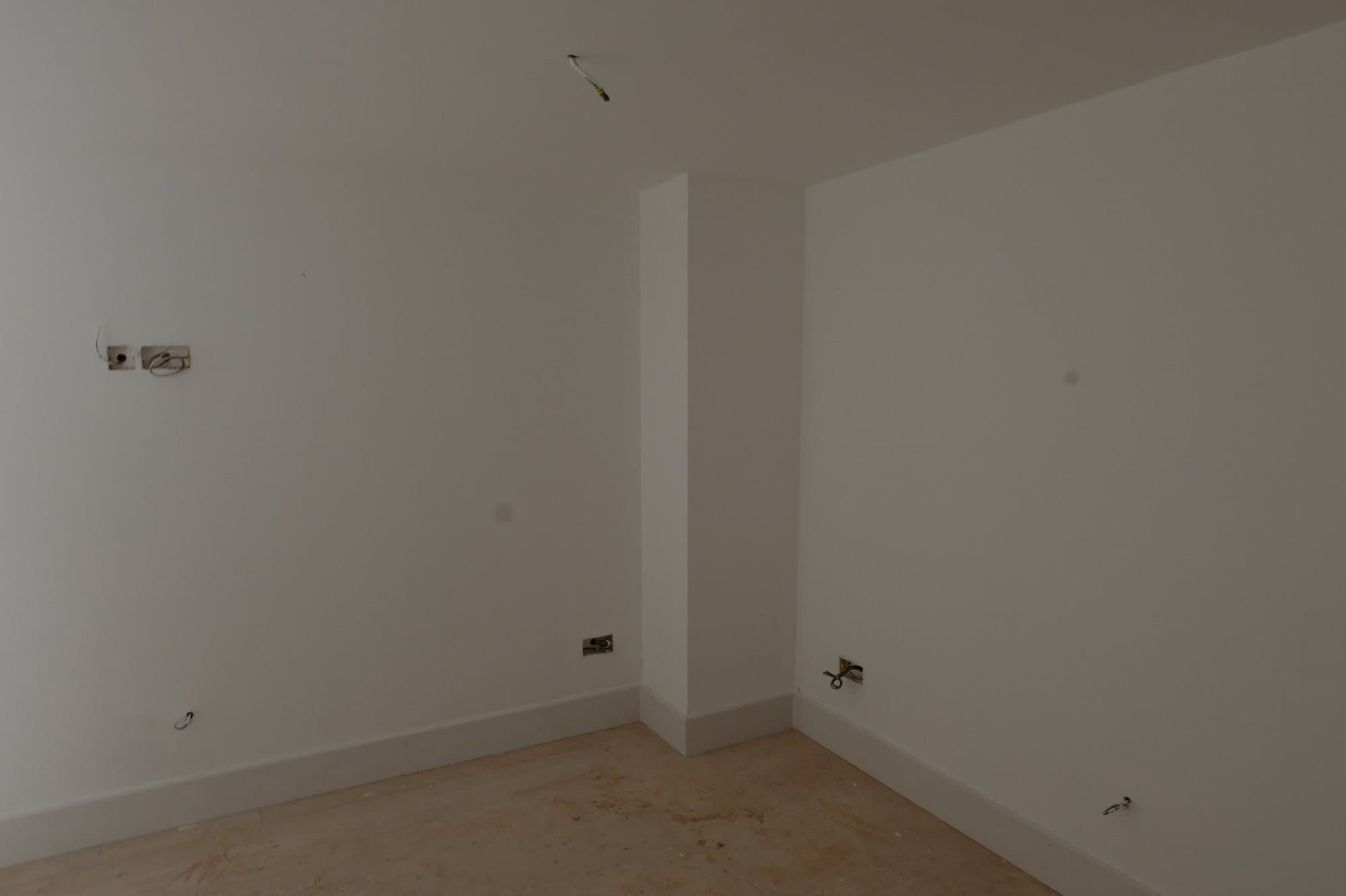 Plastered room with bare walls, exposed socket backboxes and no flooring laid yet