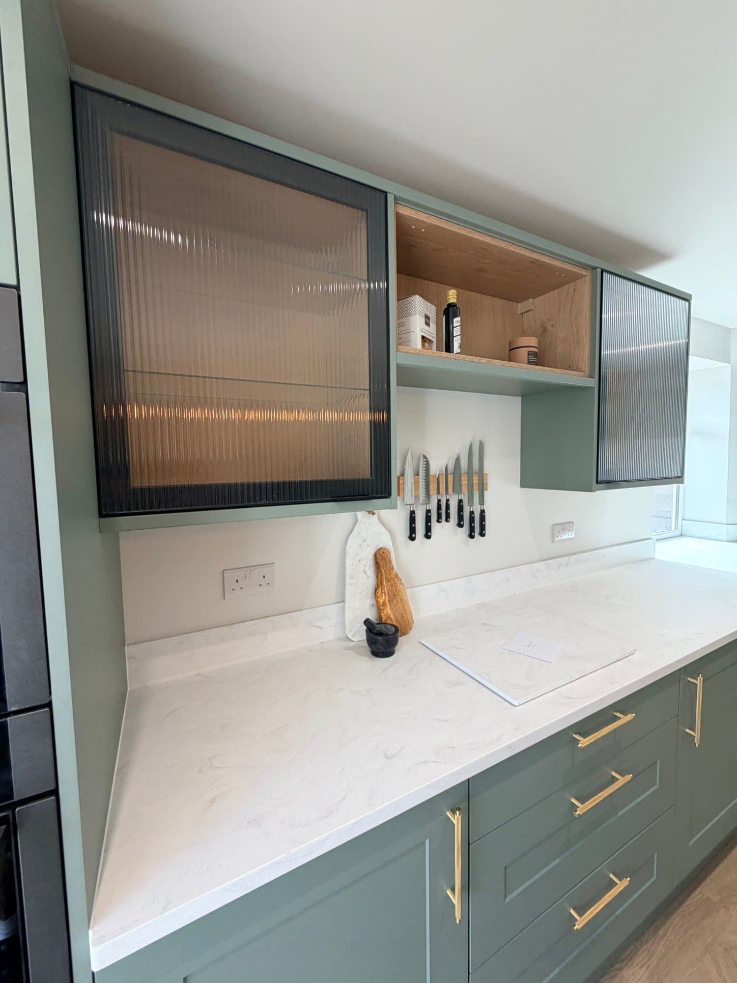 Reeded glass wall cabinets with internal oak shelving above a kitchen worktop