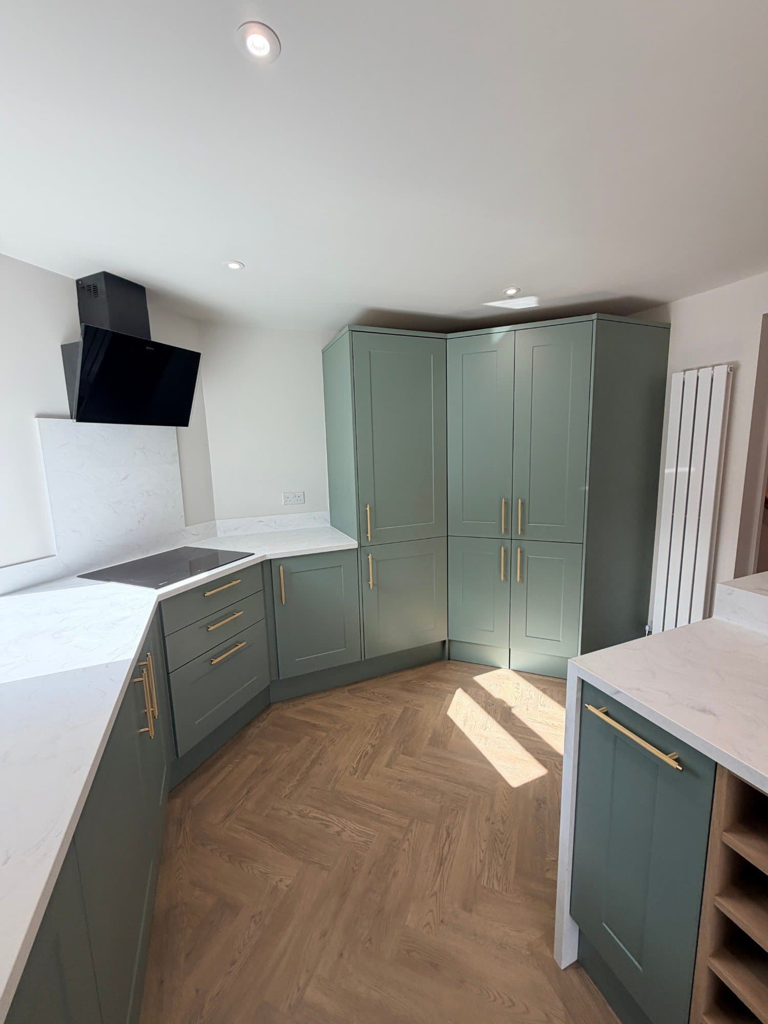 Corner larder unit and induction hob in a sage green fitted kitchen