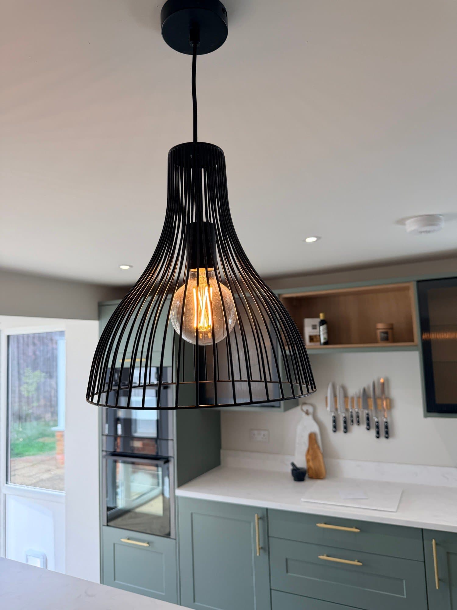 Black wire pendant light above a kitchen island, with exposed filament bulb