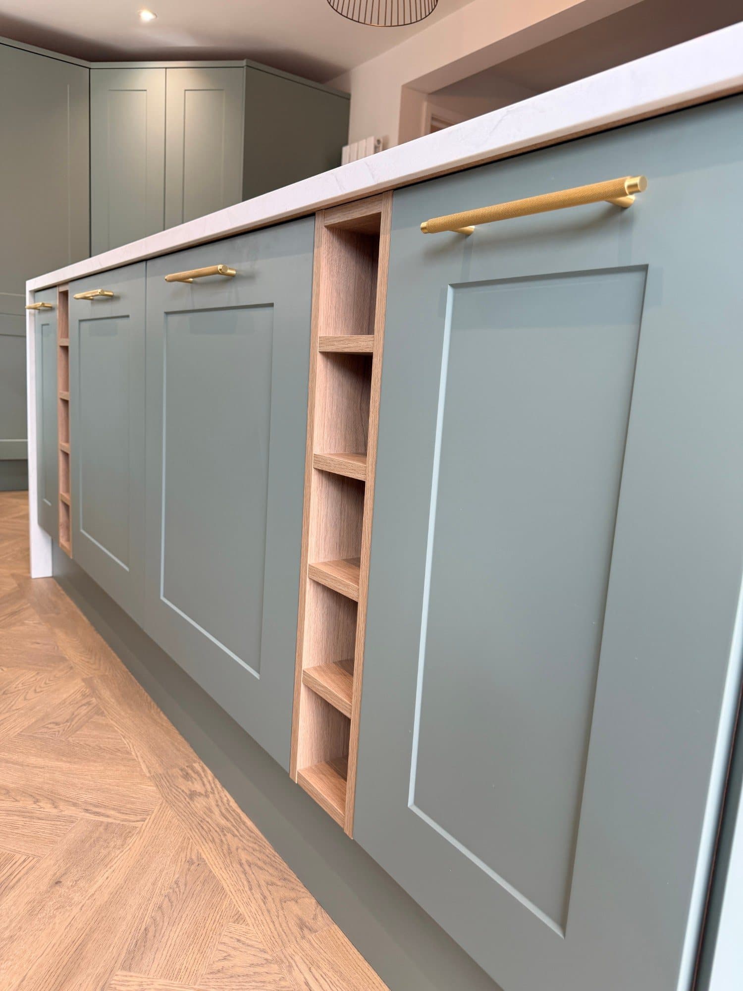 Kitchen island cabinetry with brass bar handles and oak shelving detail