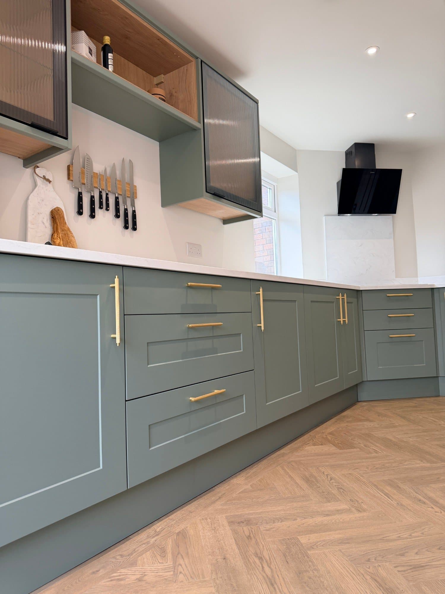Reeded glass wall cabinet and extractor hood in a sage green kitchen