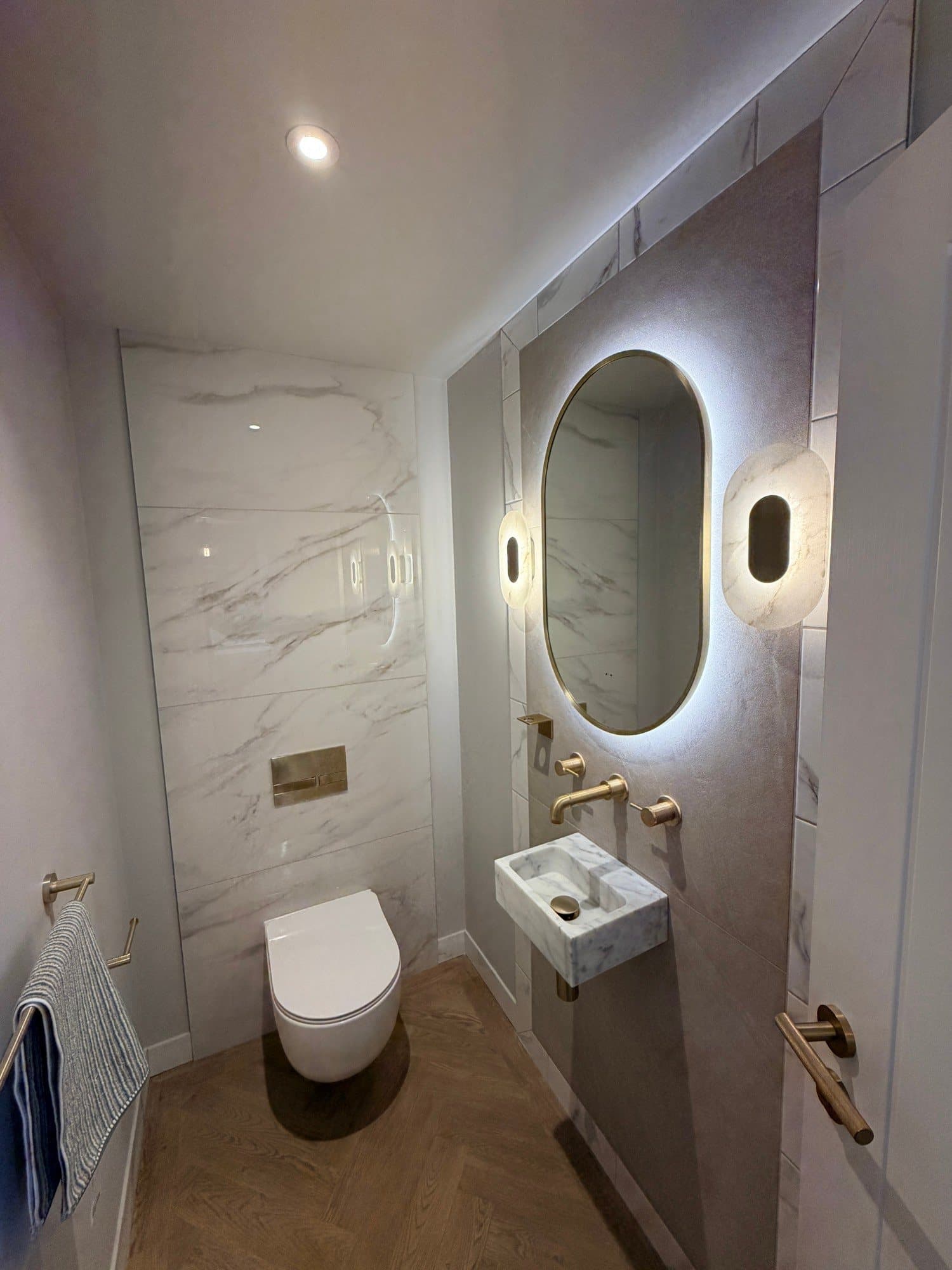 Backlit oval mirror with brass frame above a marble wall-hung basin